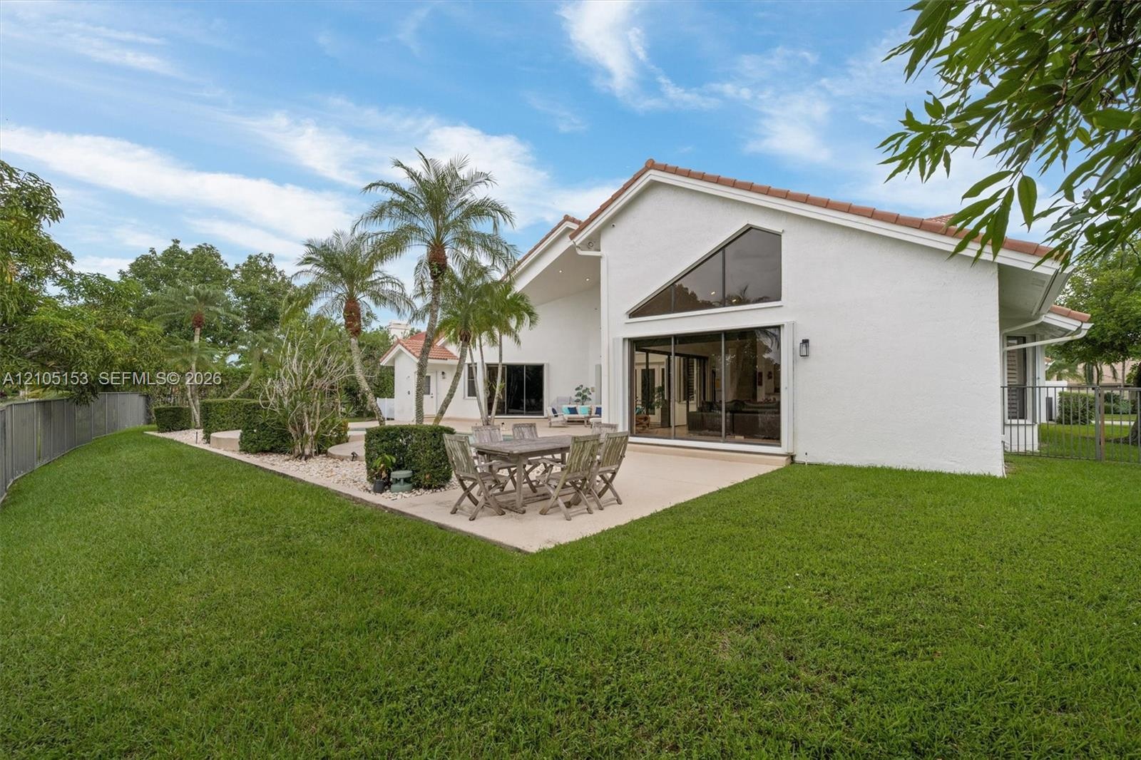 Expansive green lawn, mature palm trees, tiled roofline, large window array, and a spacious patio