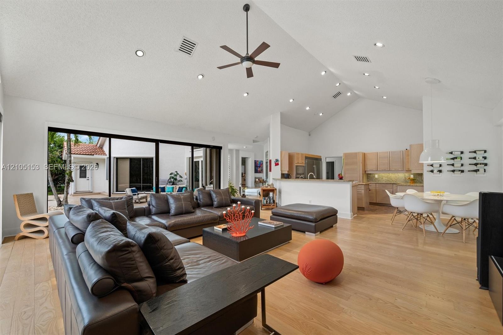 Open-concept living area featuring vaulted ceilings, recessed lighting, wood-finish flooring, and a kitchen with wood cabinetry
