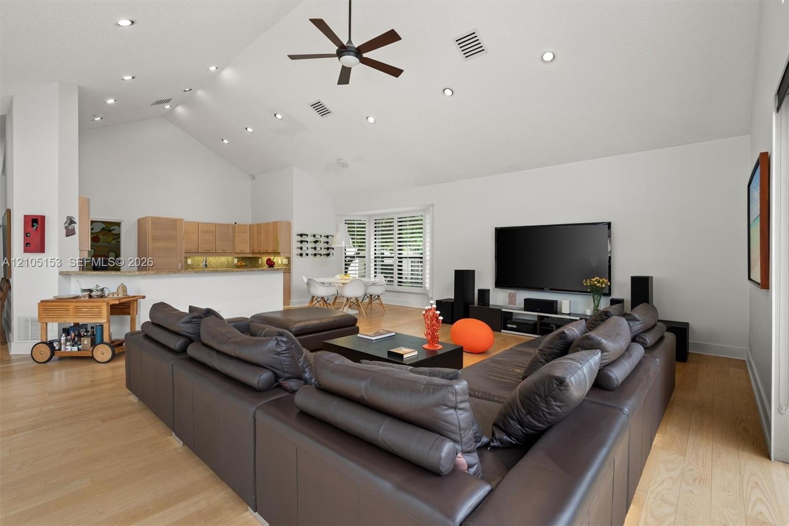 Vaulted ceiling with recessed lighting, wood-finish flooring, ceiling fan, kitchen with light wood-finish cabinetry, and a breakfast bar