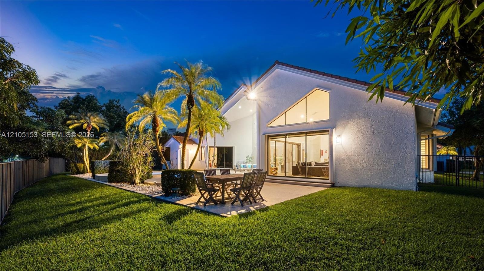 Expansive lawn with mature palm trees, a concrete patio, and large glass sliding doors