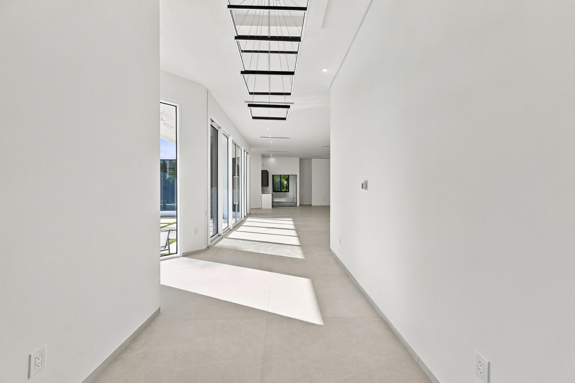 Expansive hallway featuring floor-to-ceiling glass doors, large format tile flooring, contemporary linear chandeliers, and recessed lighting