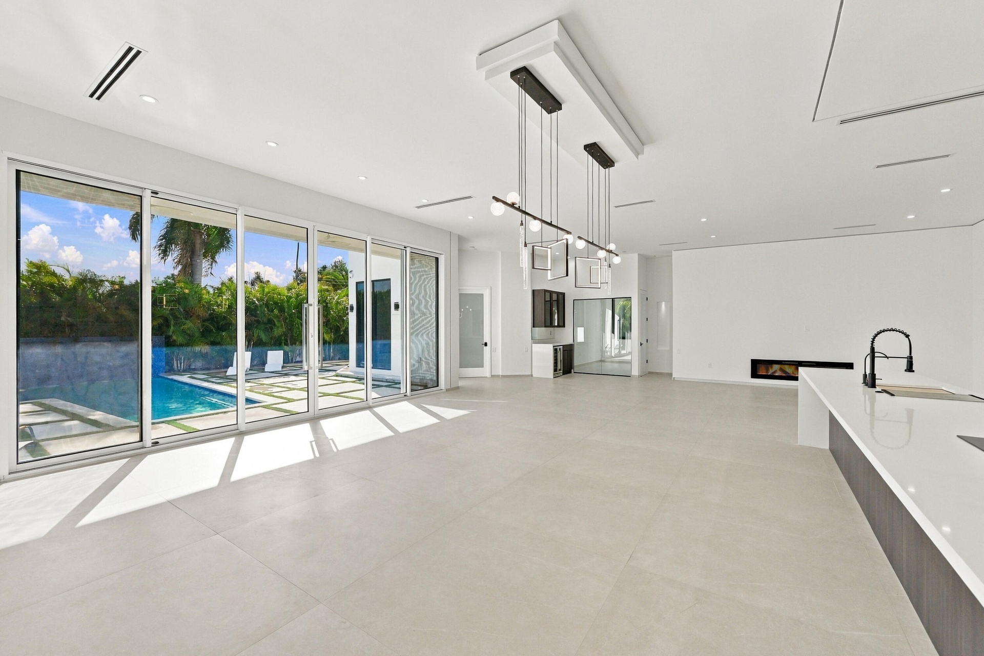 Sophisticated open-concept living space featuring polished light-toned stone flooring, floor-to-ceiling multi-panel glass doors and windows overlookin