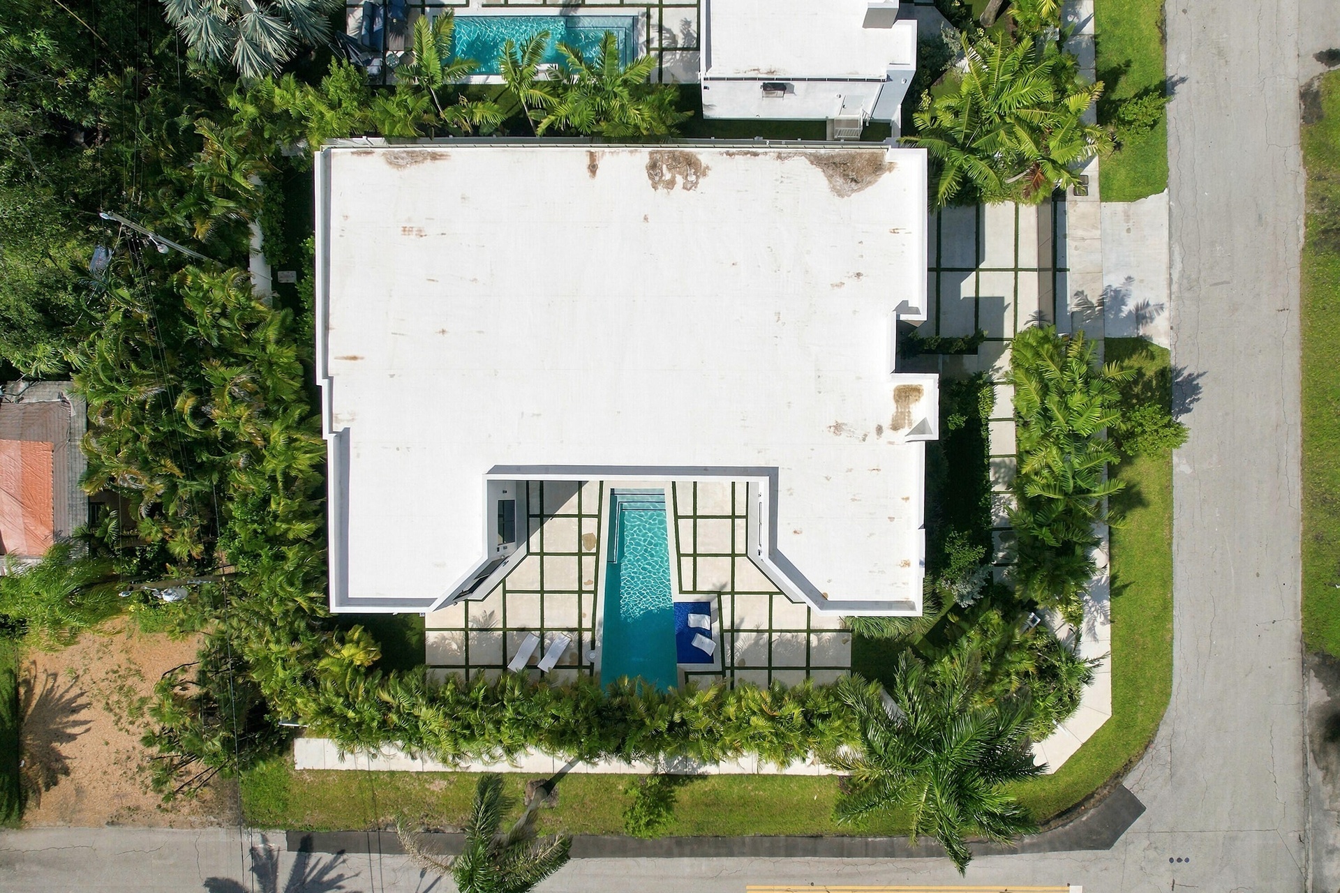 Aerial view showcasing a modern residence with a flat roof, clean white exterior, and a striking turquoise swimming pool surrounded by a dark-finished