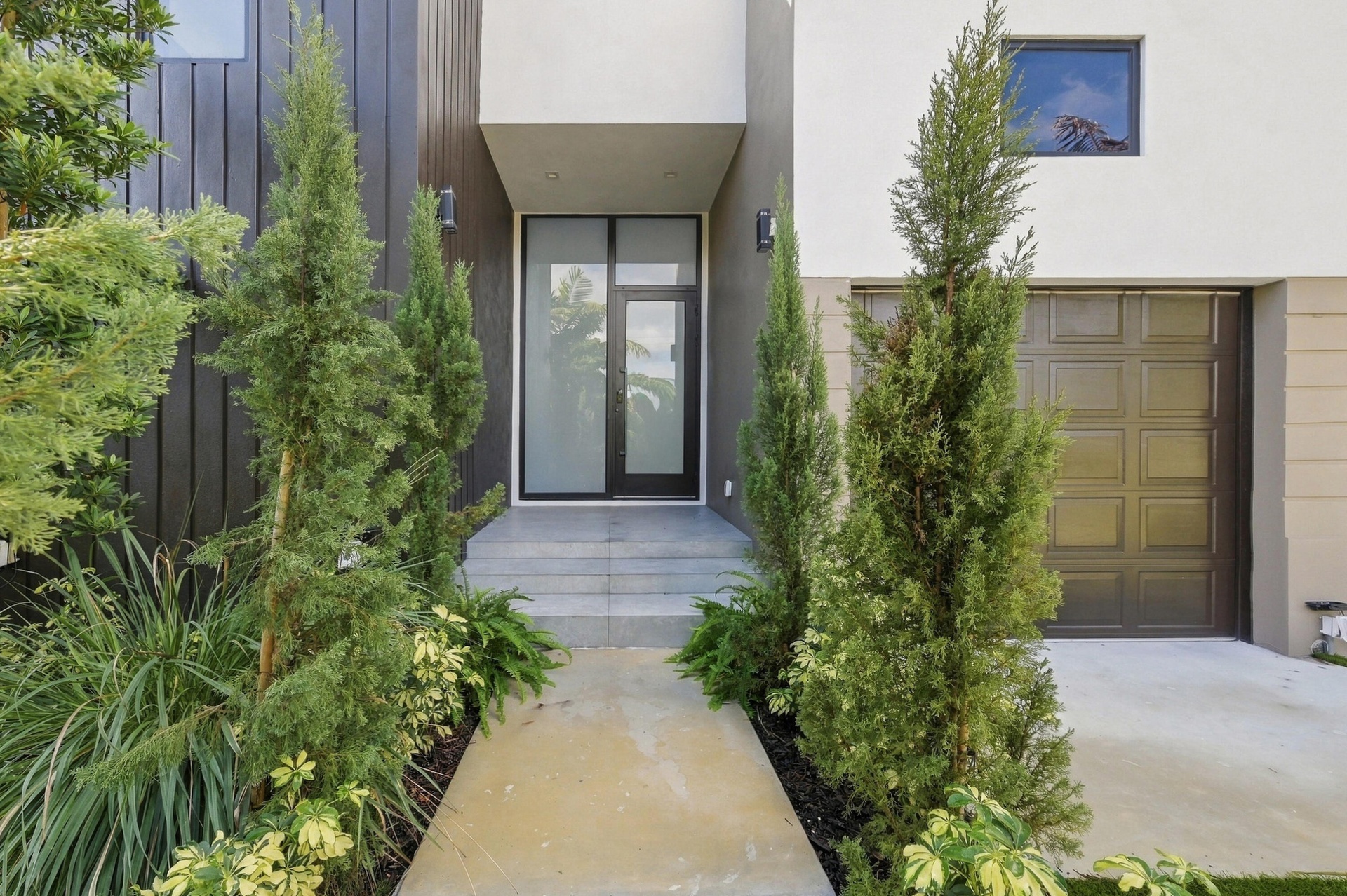 Modern exterior featuring black vertical siding, a white stucco finish, a paneled garage door, a glass entry door, and concrete steps