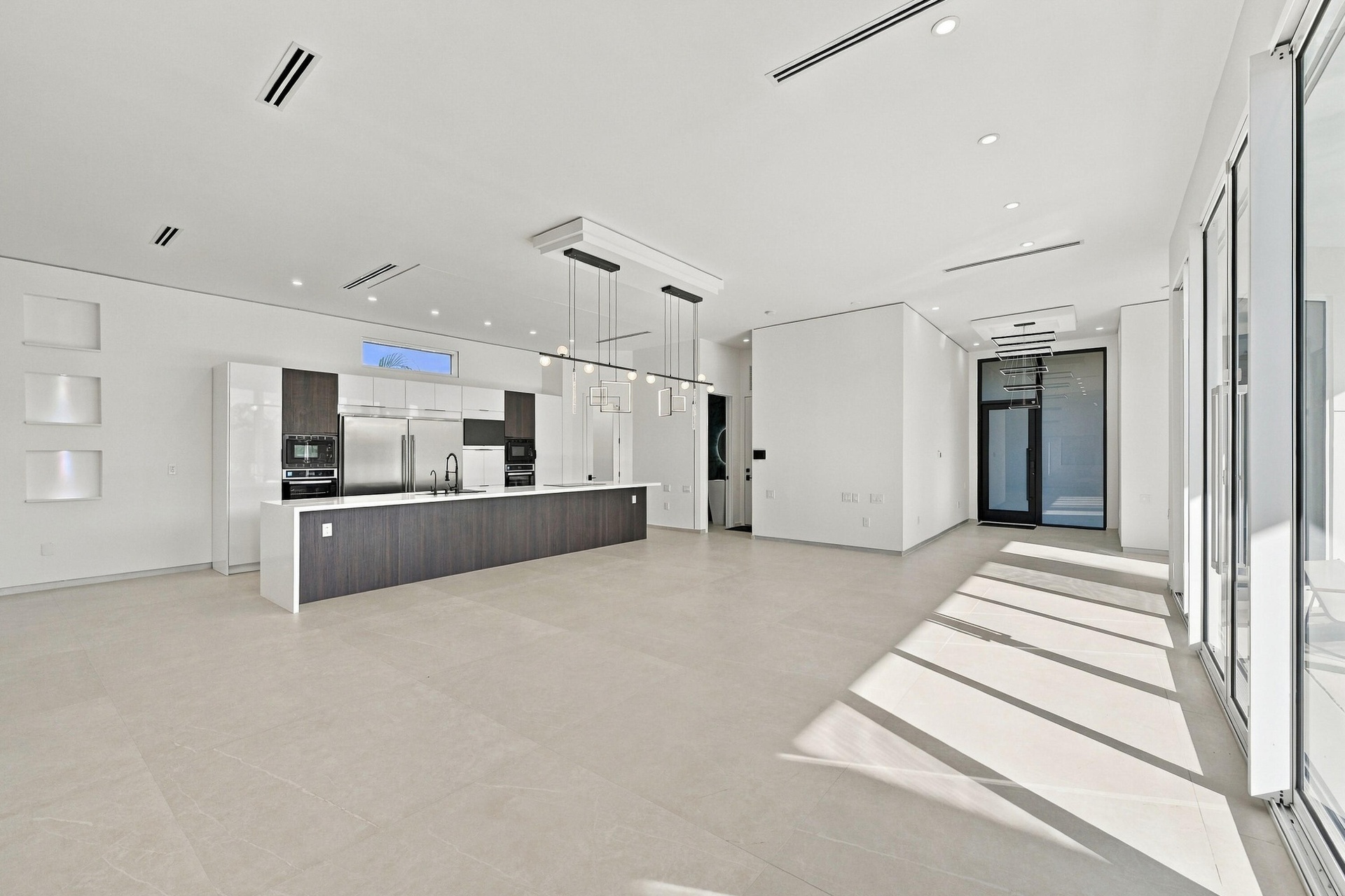 Spacious open-concept interior featuring light-toned flooring, a full-height glass door, and recessed lighting