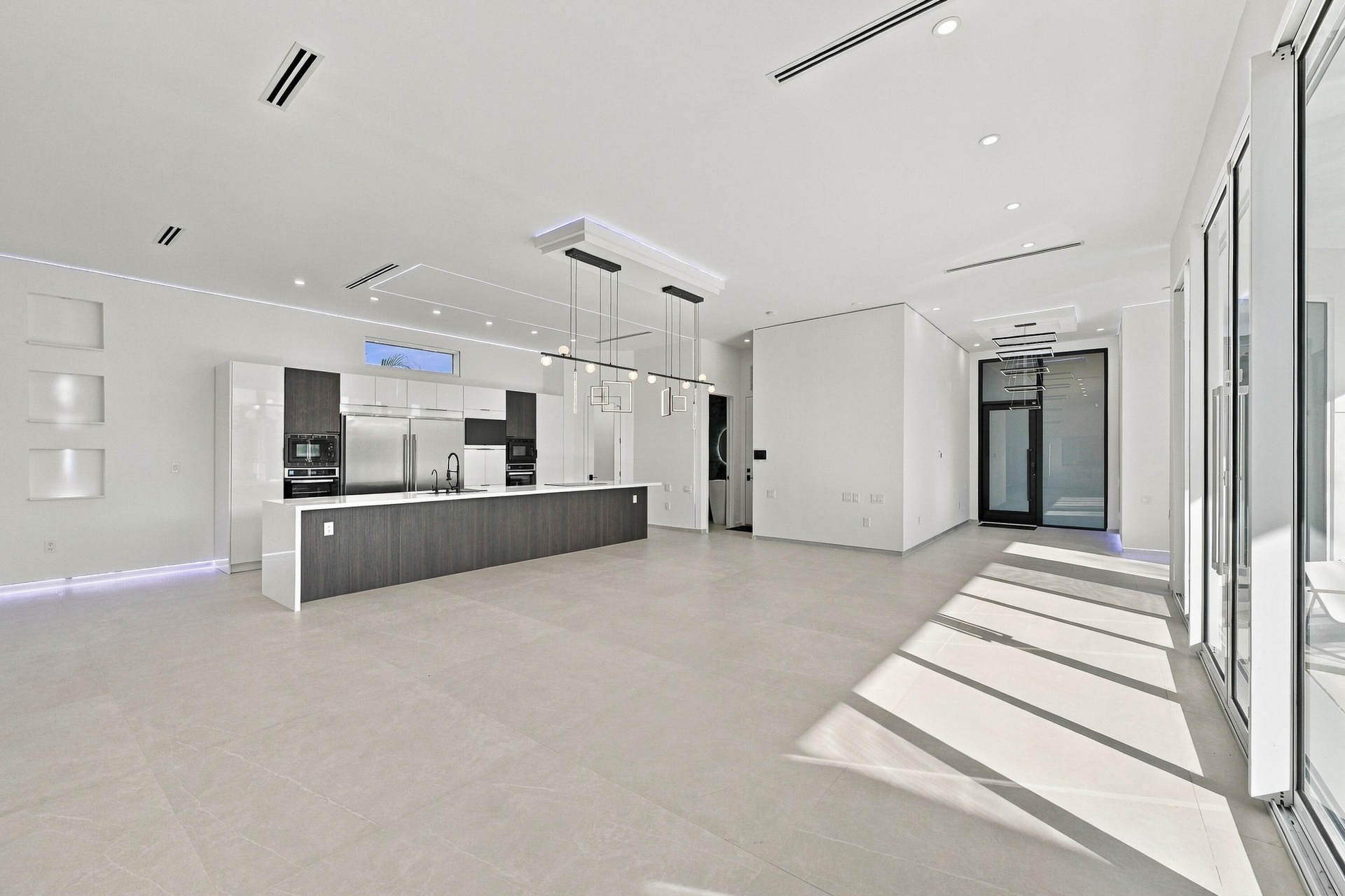 Modern open-concept living space featuring polished concrete flooring, recessed ceiling lighting, and expansive glass sliding doors flooding the area 