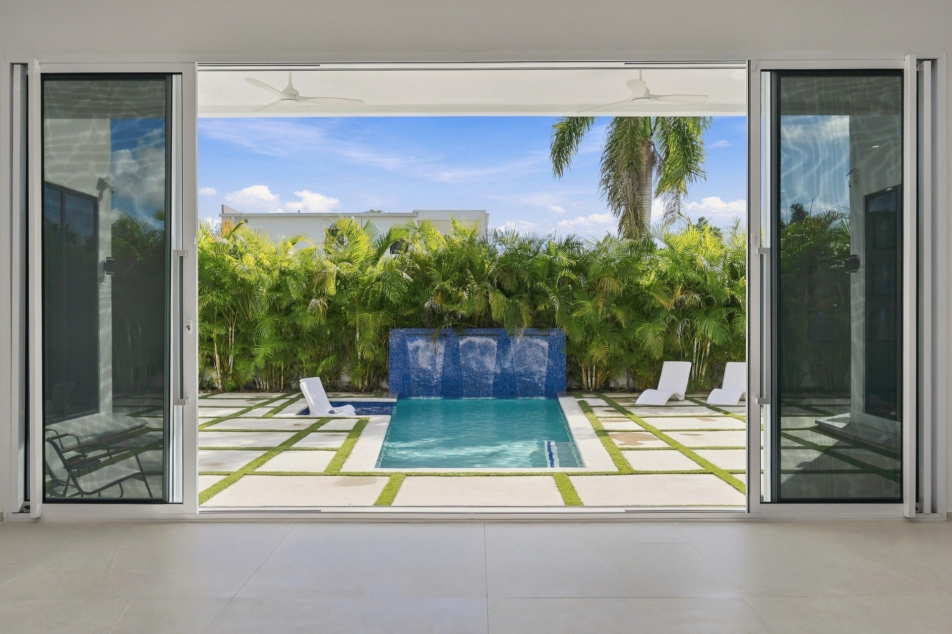 Seamless indoor-outdoor living with floor-to-ceiling glass doors opening to a resort-style backyard featuring a geometric paved terrace, resort pool w
