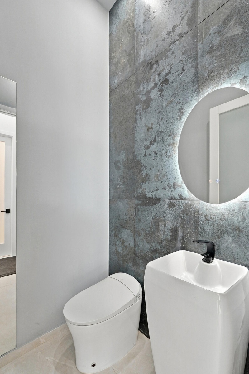 Modern bathroom featuring a sleek vessel sink with matte black wall-mounted faucet, illuminated circular mirror with integrated lighting, and a contem