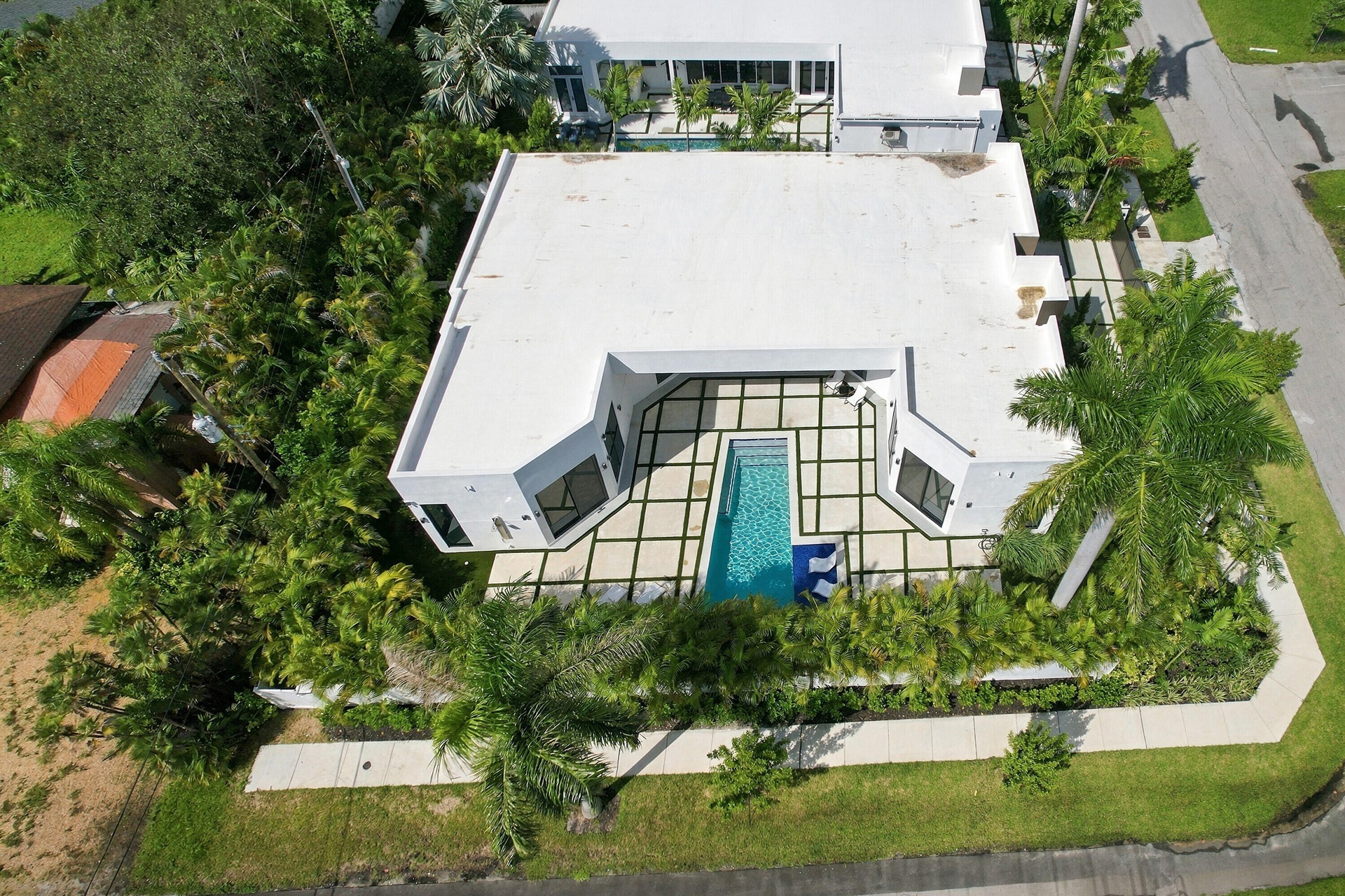Aerial view showcasing a modern residence with a striking screened pool enclosure featuring black framing, surrounded by mature landscaping and lush g