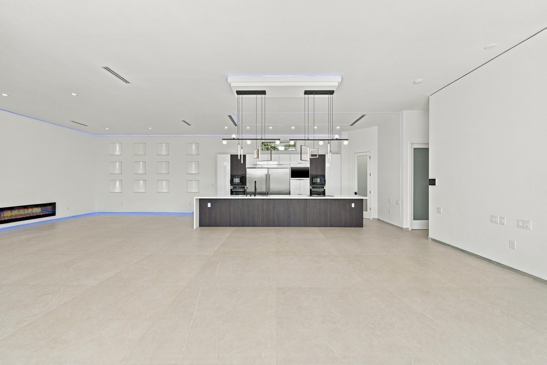 Expansive open-concept space featuring light wood-finish flooring, recessed ceiling lighting, and a contemporary dark-finished bar counter with integr