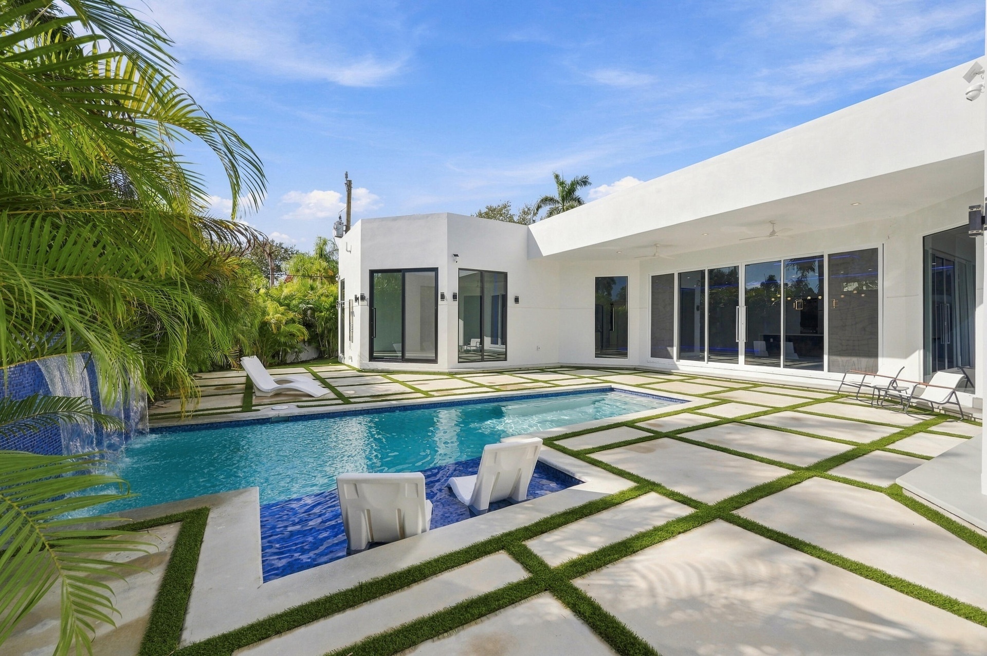 Modern residence featuring a resort-style swimming pool with crystal-clear waters, expansive hardscape patio with geometric inset planting beds, matur