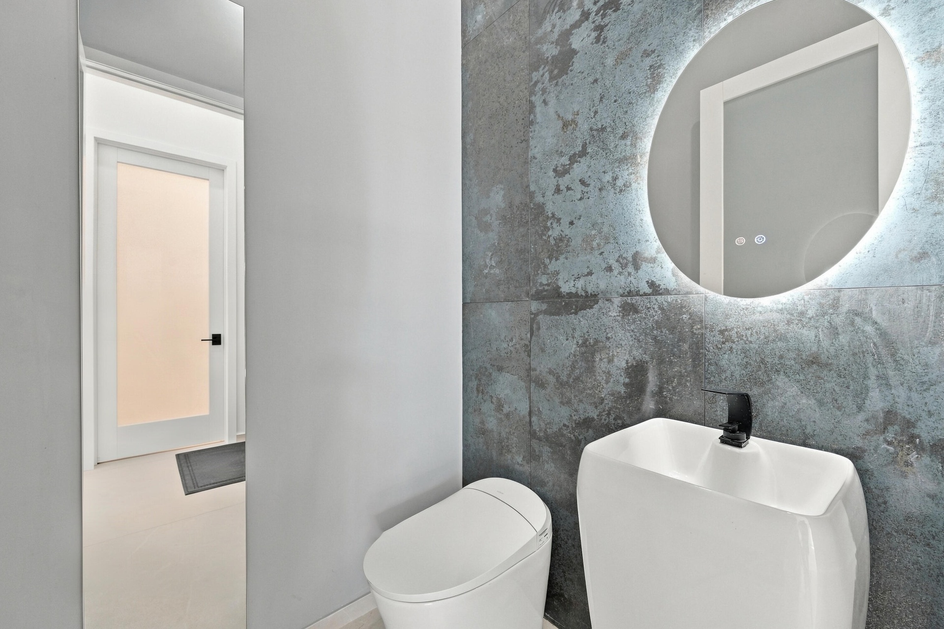 Modern bathroom featuring a sleek ceramic vessel sink with matte black faucet, illuminated circular mirror with integrated LED lighting, and polished 