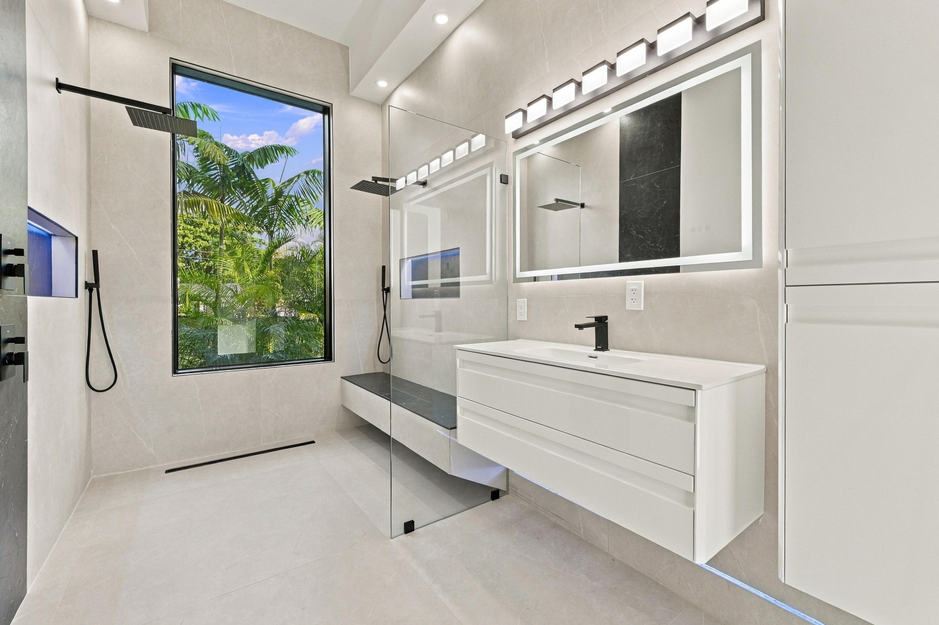Spa-inspired primary bathroom featuring a frameless glass-enclosed shower with rainfall showerhead and handheld fixture, floating vanity with integrat
