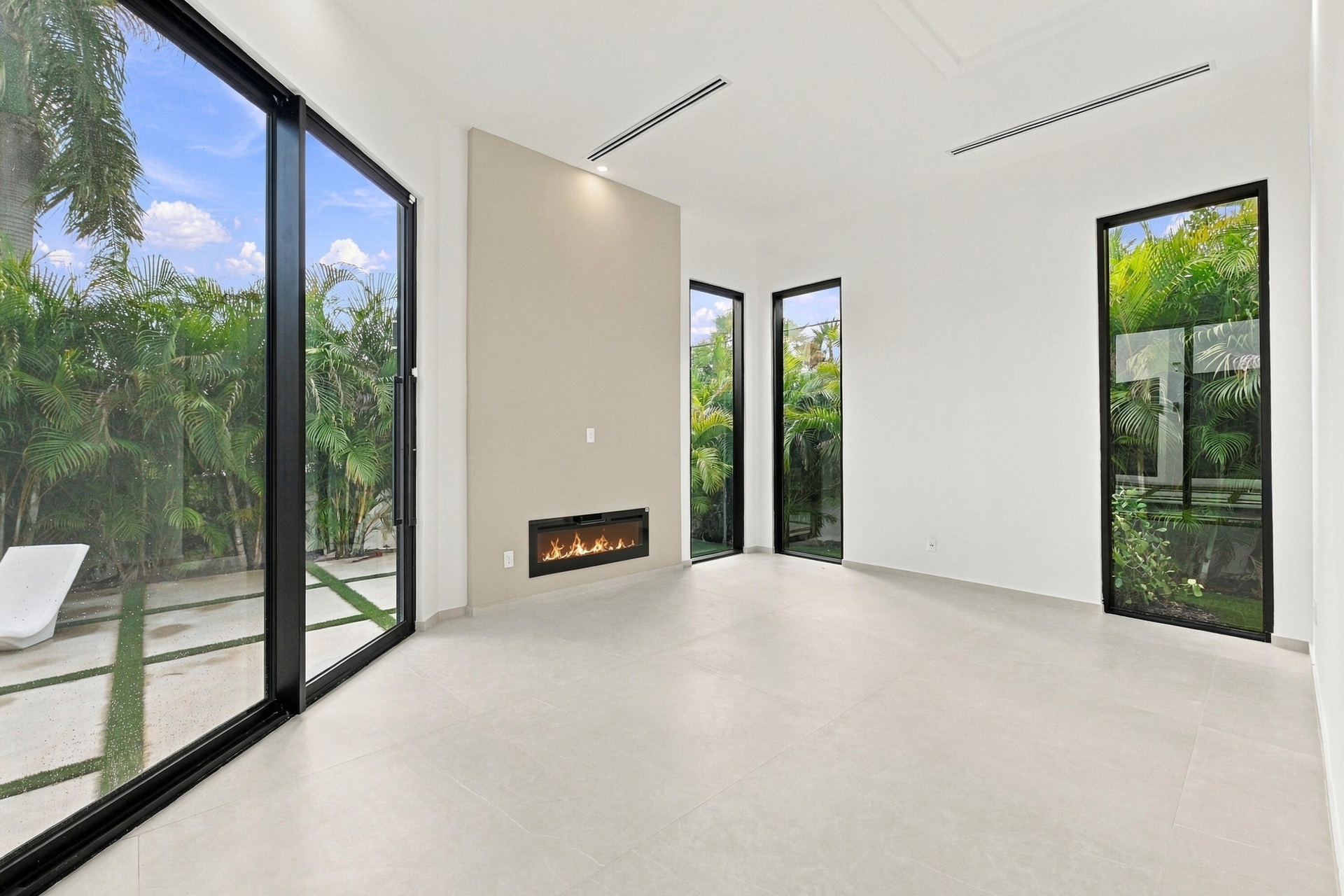 Bright, open interior featuring polished concrete flooring, floor-to-ceiling glass sliding doors with black frames, linear fireplace with stone surrou