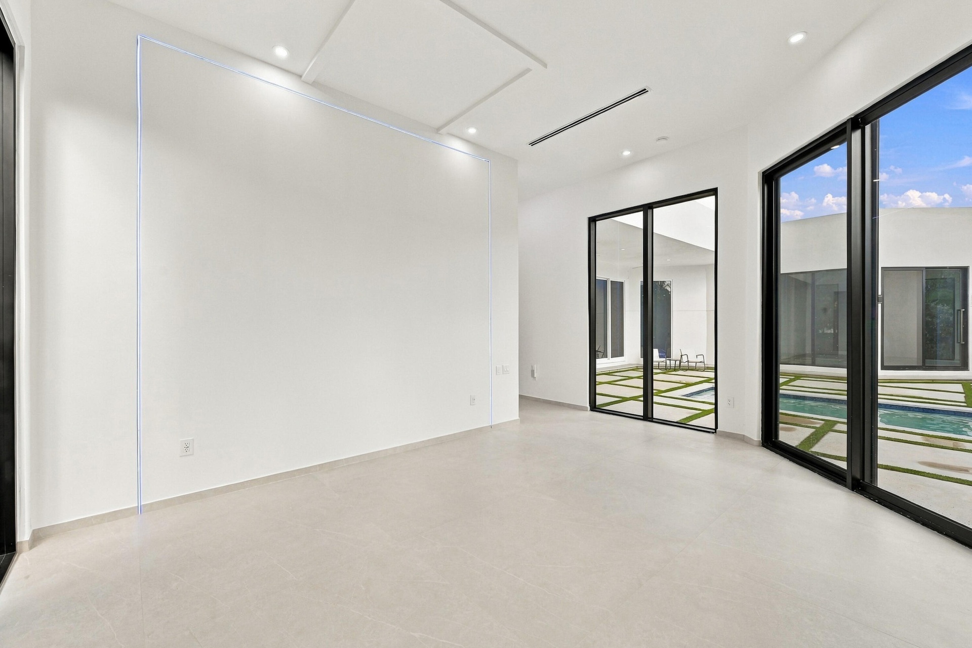 Bright, open interior space featuring polished concrete flooring, floor-to-ceiling glass doors with black aluminum framing, and recessed ceiling light