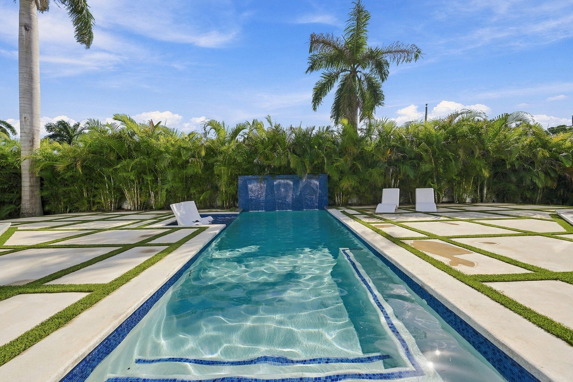 Resort-style lap pool with lane markers and deep blue tile accents, flanked by manicured lawn strips and mature palm landscaping