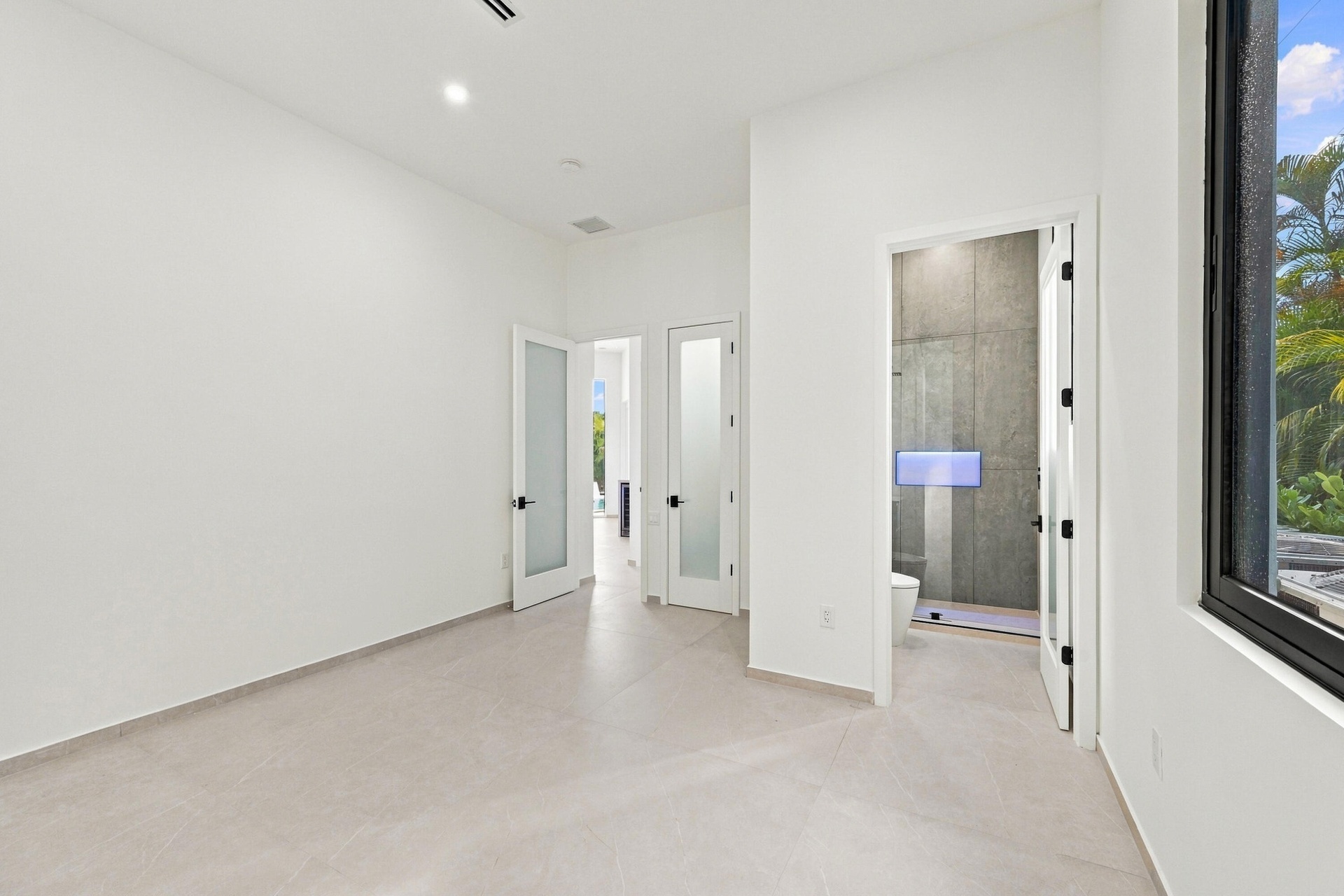 Bright, open primary suite featuring polished concrete flooring, multiple glass-panel French doors with black hardware, recessed ceiling lighting, and