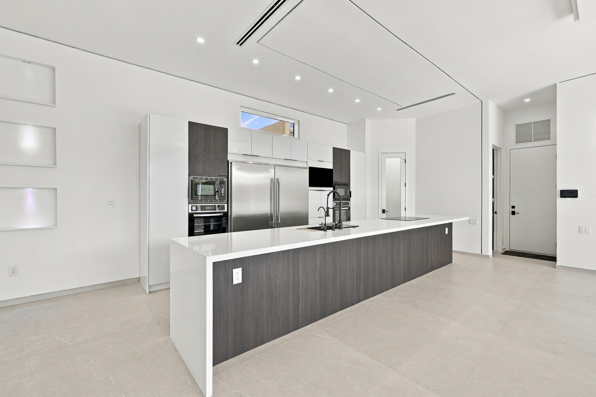 Modern kitchen featuring a large waterfall-edge island with wood-finish cabinetry, stainless steel appliances including a built-in refrigerator and wa
