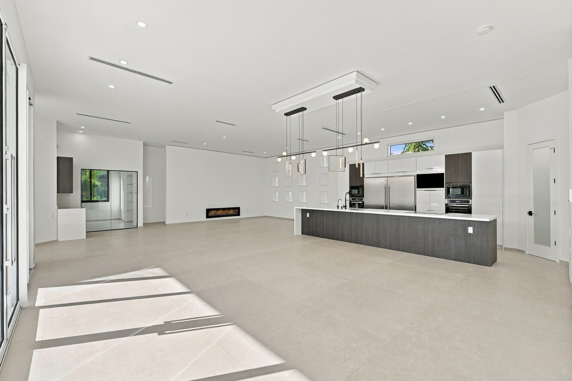 Spacious open-concept living area featuring polished concrete flooring, recessed and pendant lighting throughout, and a modern kitchen with dark cabin