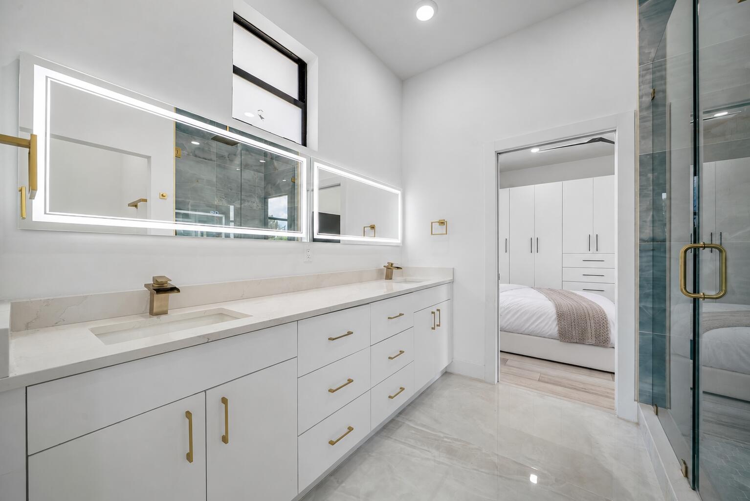 Spacious Jack-and-Jill bathroom featuring a glass-enclosed shower with blue-toned tile, a dual vanity with light-colored countertops, white cabinetry 