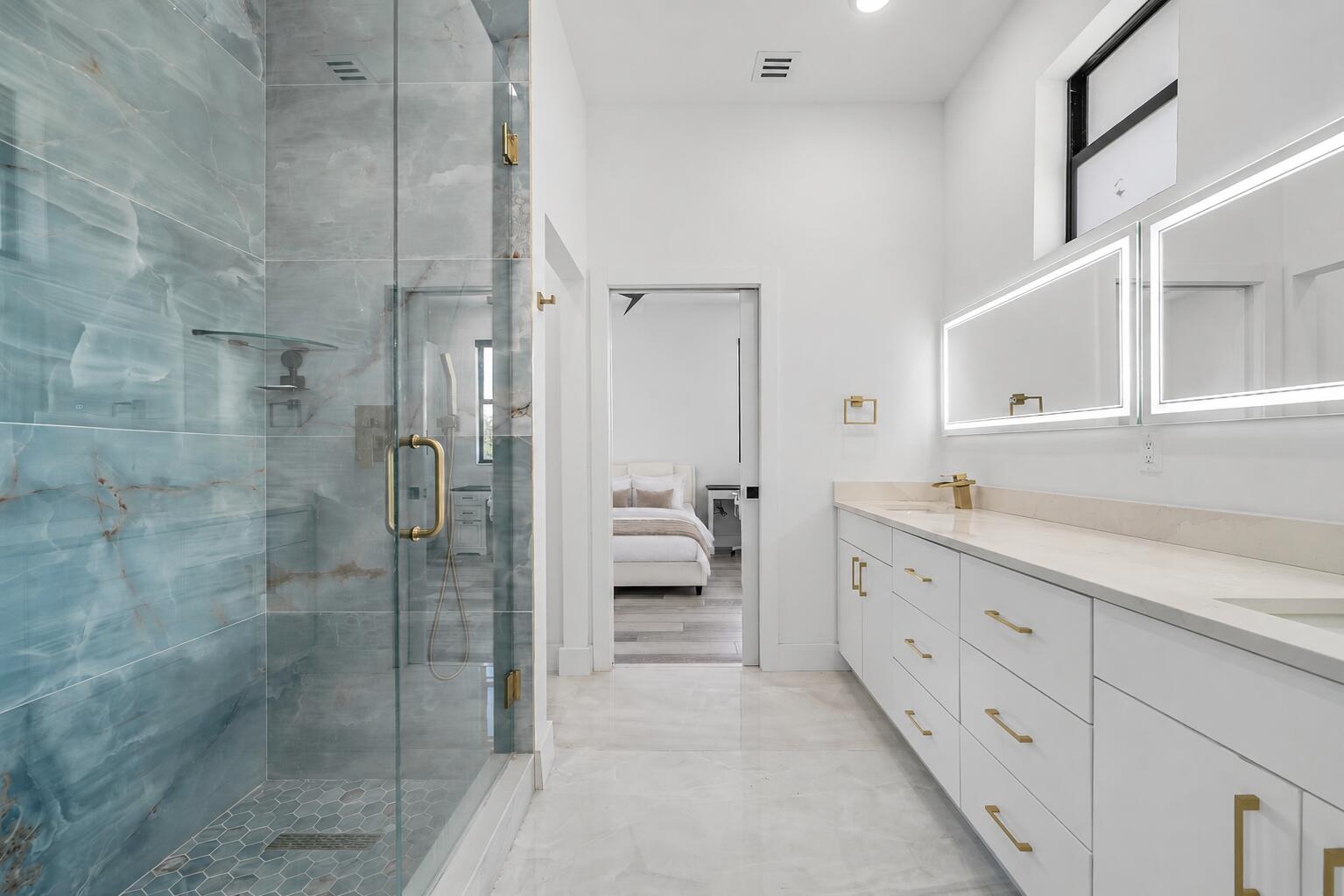 Jack-and-Jill bathroom featuring dual vanity with quartz countertops and integrated sinks, illuminated mirrors, frameless glass shower enclosure, and 
