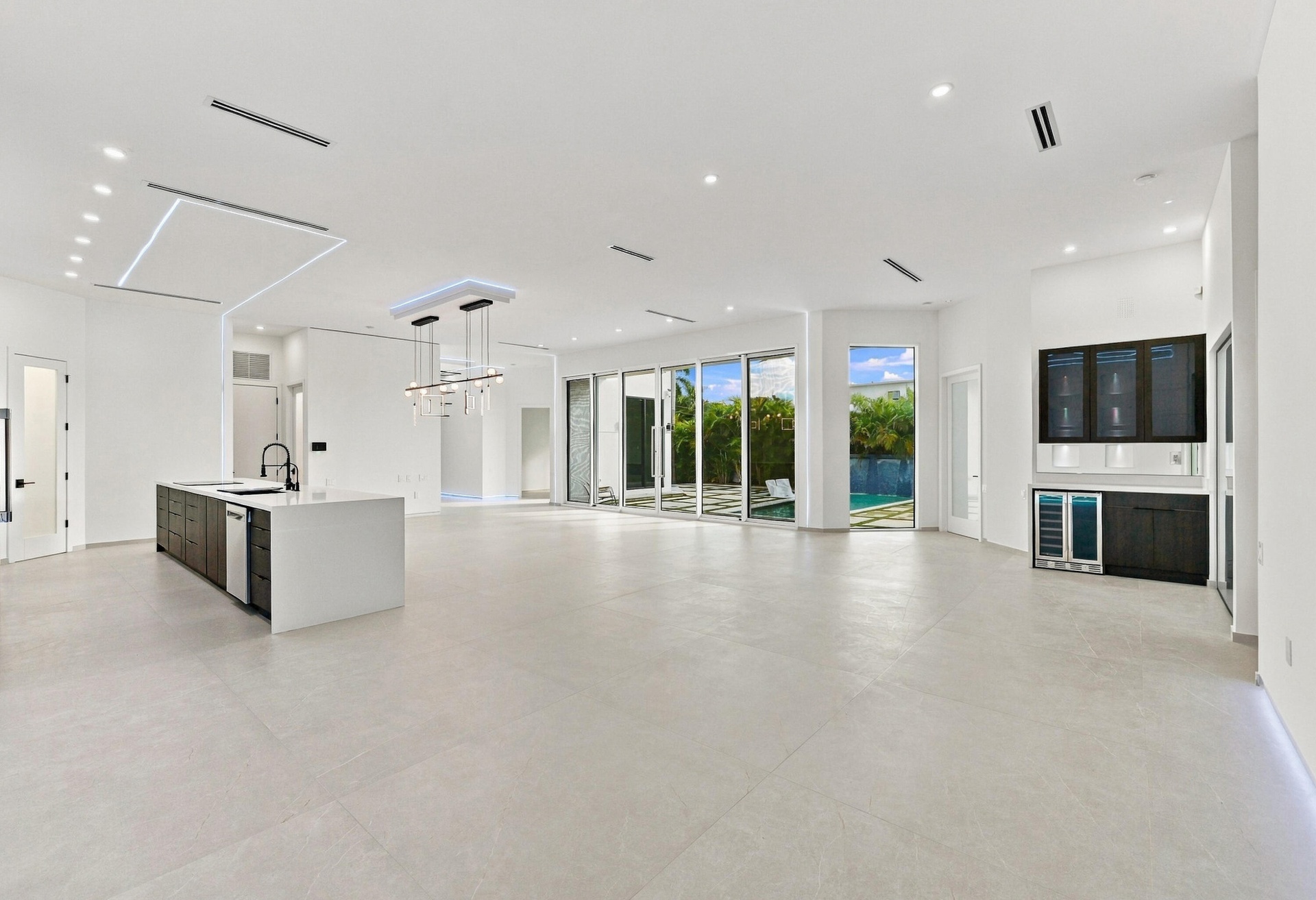 Expansive open-concept living space featuring polished light-toned flooring throughout, abundant natural light from multiple glass sliding doors and w