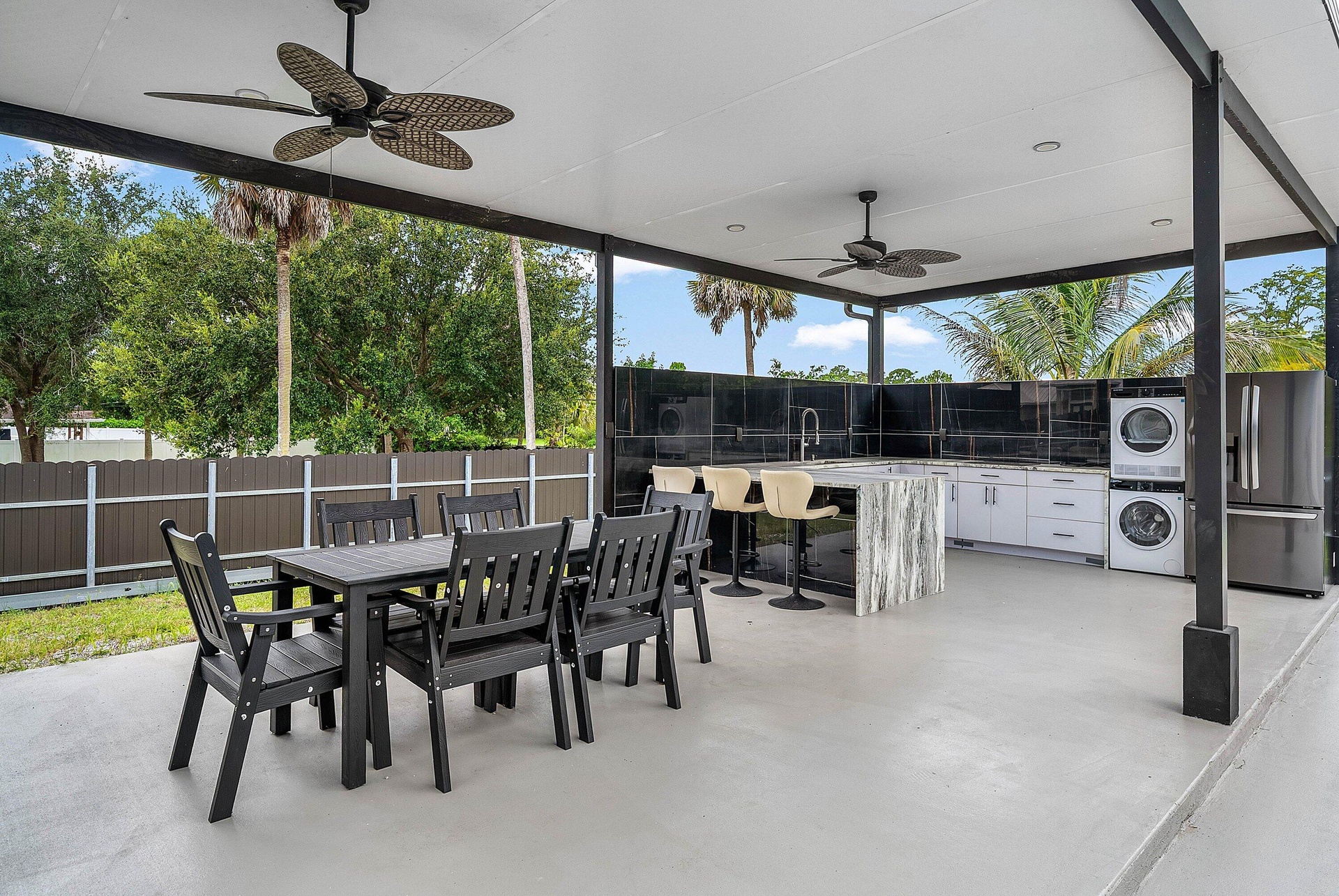 Expansive covered patio with an outdoor kitchen, featuring a central island with a sink, white cabinetry, and a dark tiled backsplash