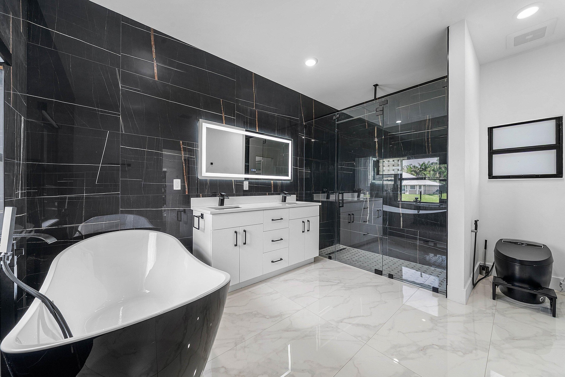 Freestanding soaking tub, dual vanity with undermount sinks, walk-in shower with glass enclosure, large format black tile accent wall, and white tile 