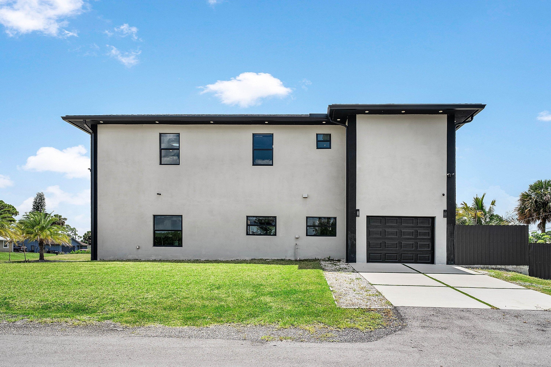 Contemporary exterior with light-colored stucco finish, dark trim details, a two-car garage, and a concrete driveway