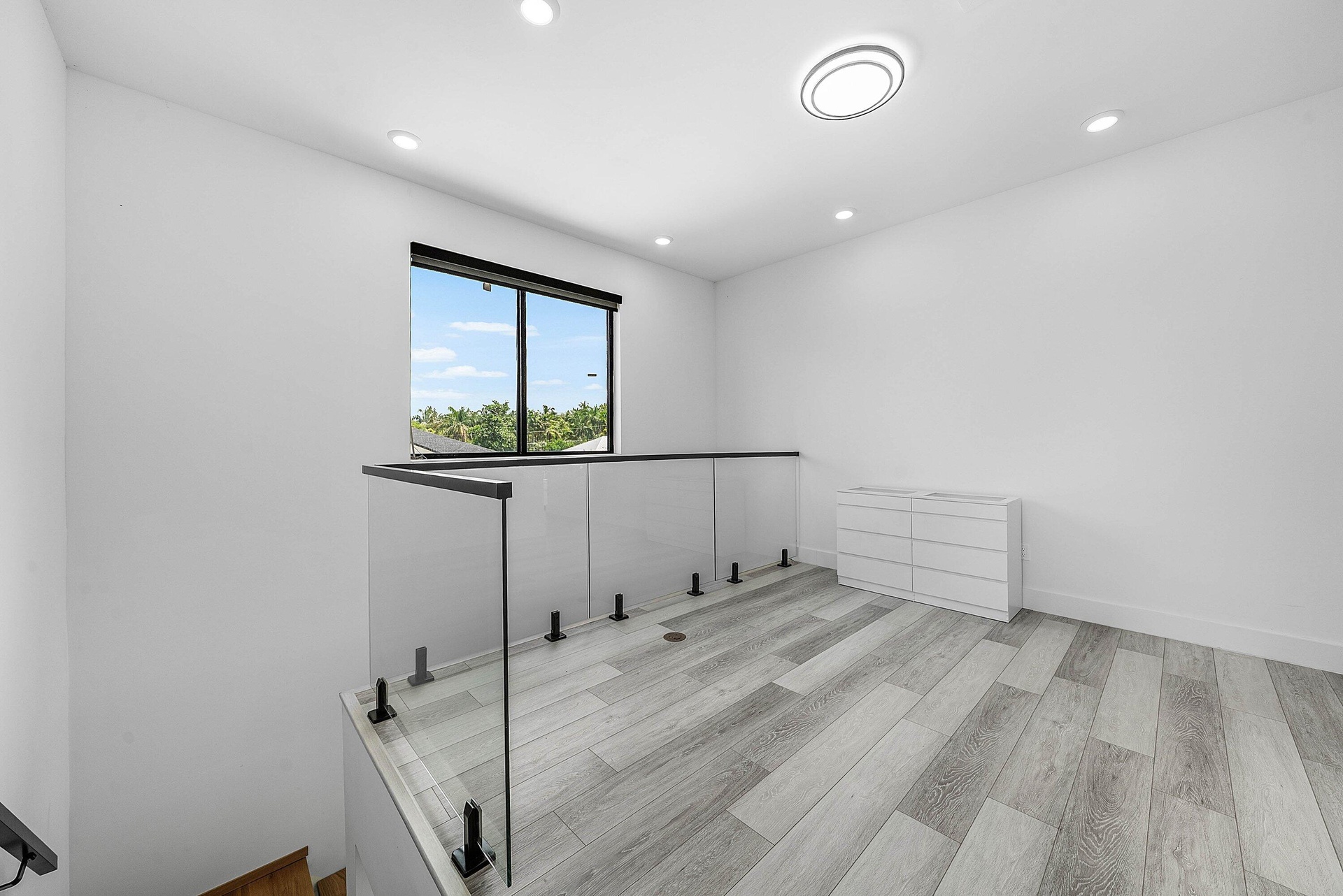 Upper-level landing featuring wood-finish flooring, glass railing, recessed lighting, and a contemporary ceiling fixture