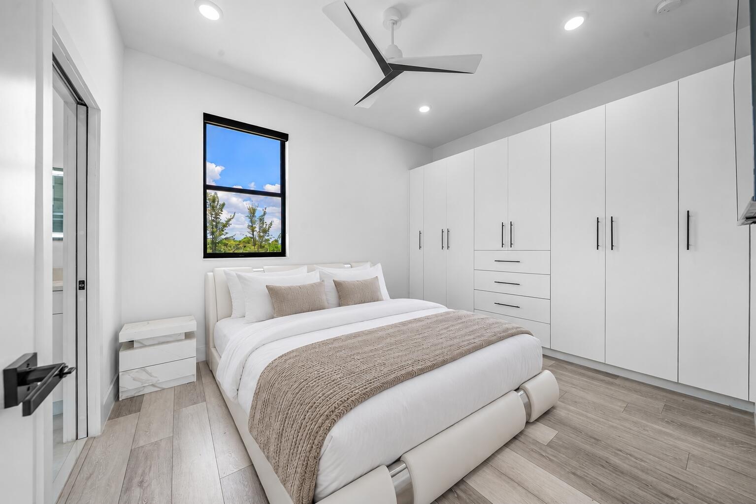 Expansive built-in wardrobe system with ample storage, contemporary ceiling fan, recessed lighting, wood-finish flooring, and multiple windows