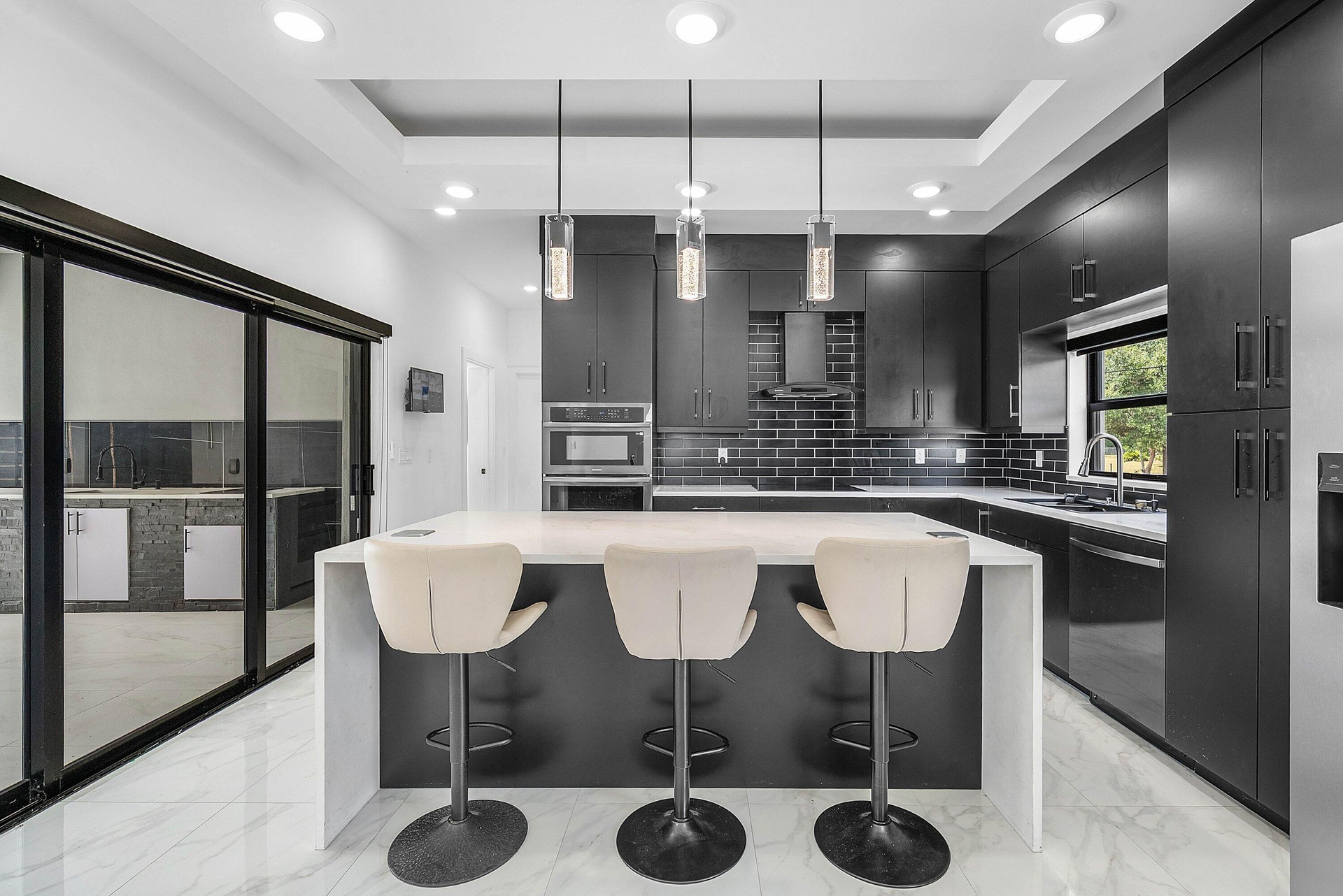 Contemporary kitchen featuring a large center island, dark cabinetry, sleek backsplash tiling, and integrated stainless steel appliances
