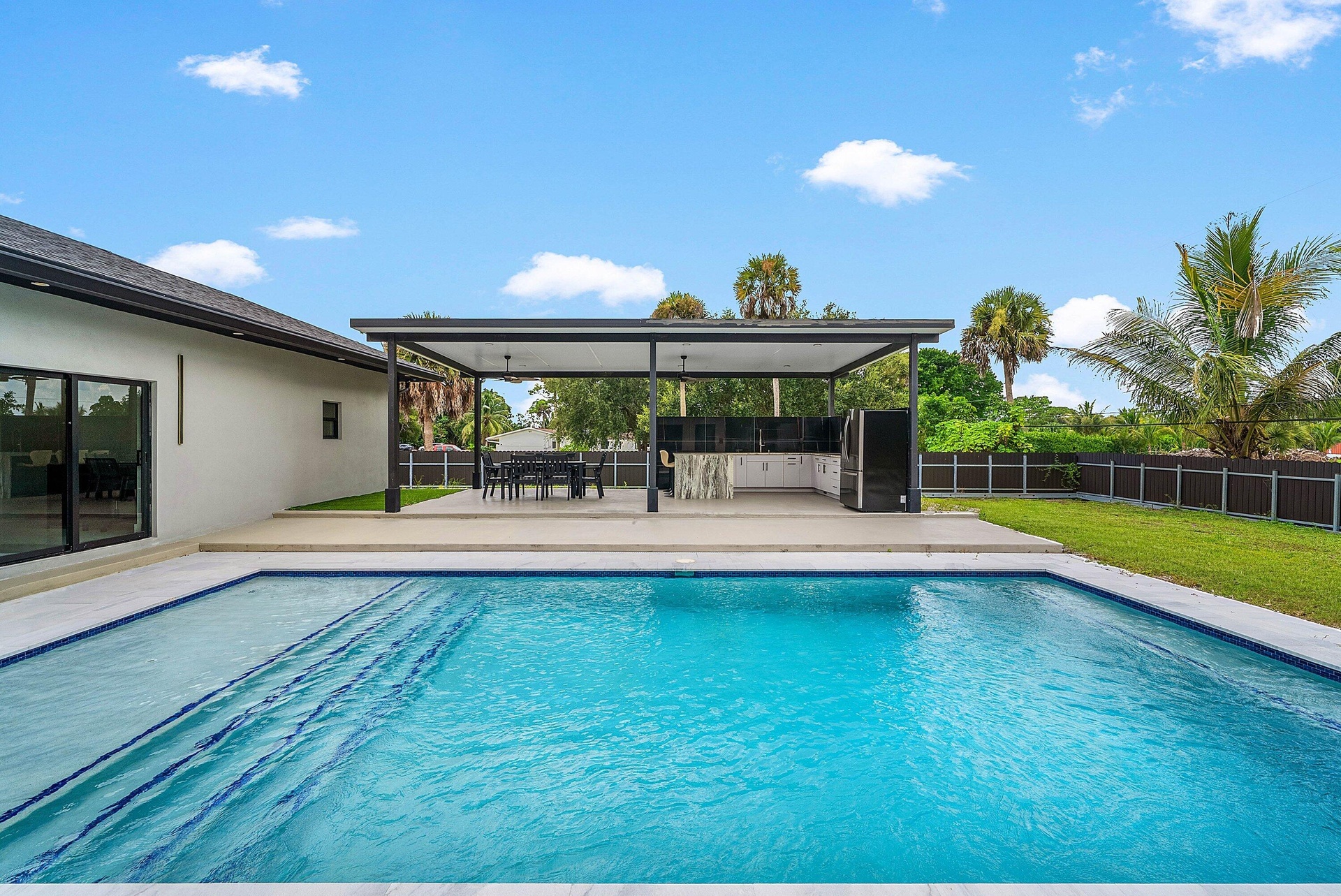 Rectangular swimming pool with integrated steps, adjacent to a covered patio featuring an outdoor kitchen