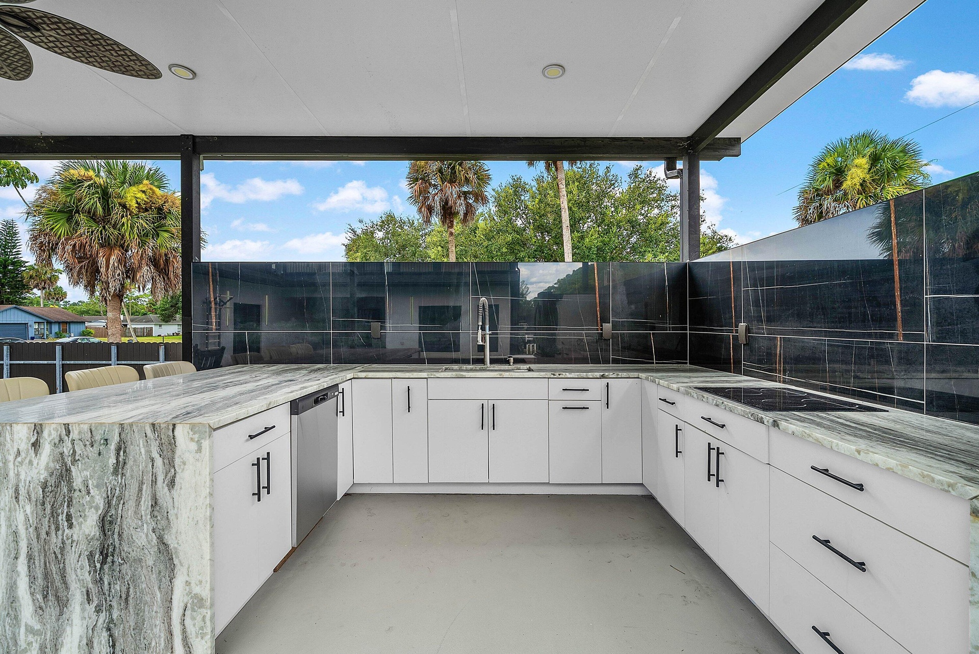 Outdoor kitchen featuring white cabinetry, a built-in cooktop, integrated dishwasher, and a bar seating area