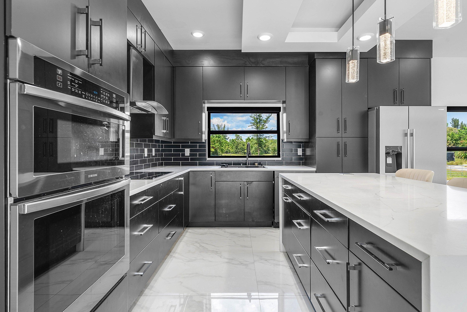 Kitchen with dark cabinetry, white countertops, built-in double oven, stainless steel appliances, and sleek pendant lighting