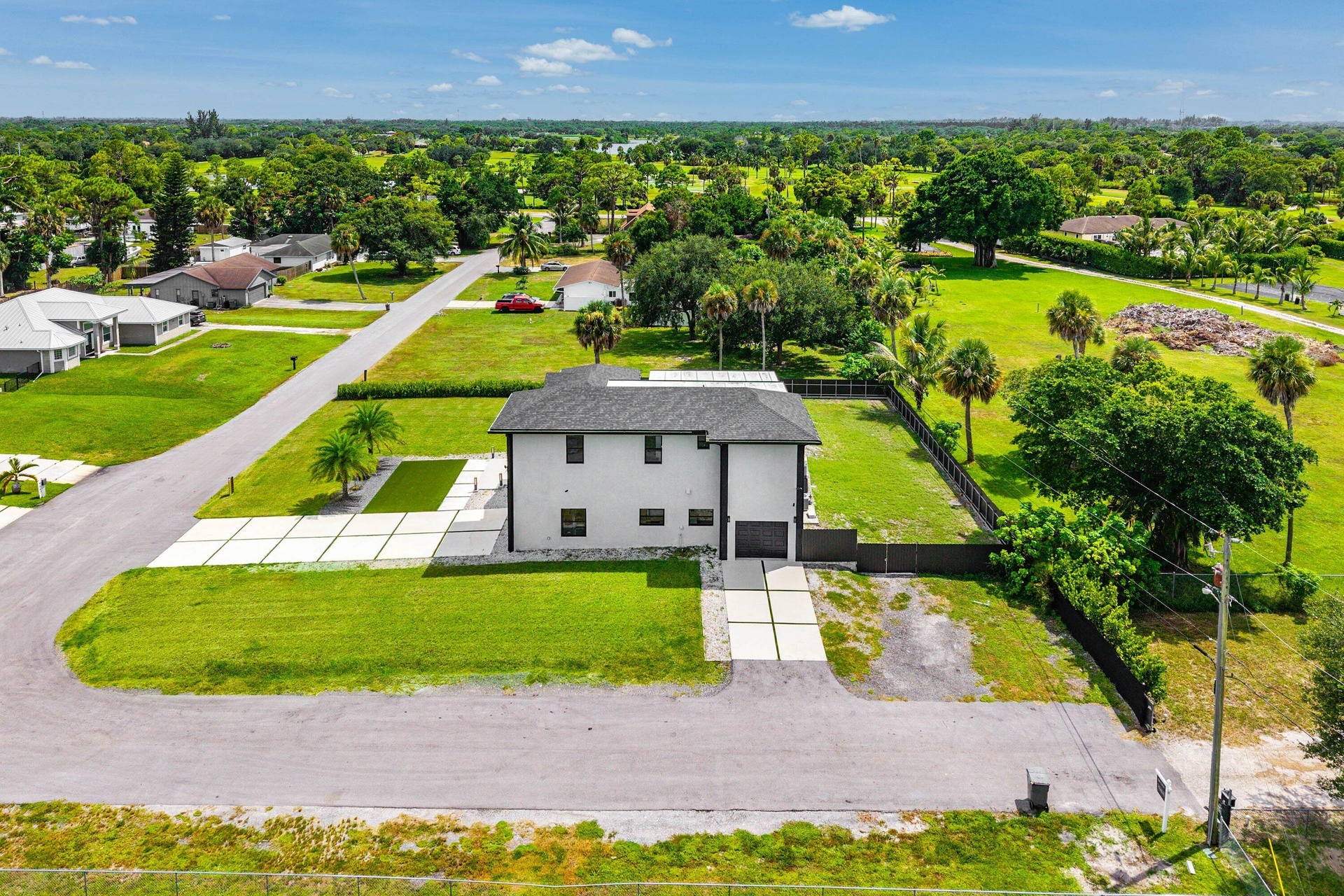 Two-story stucco exterior, dark roof, expansive green lawn, modern concrete driveway, and black fencing