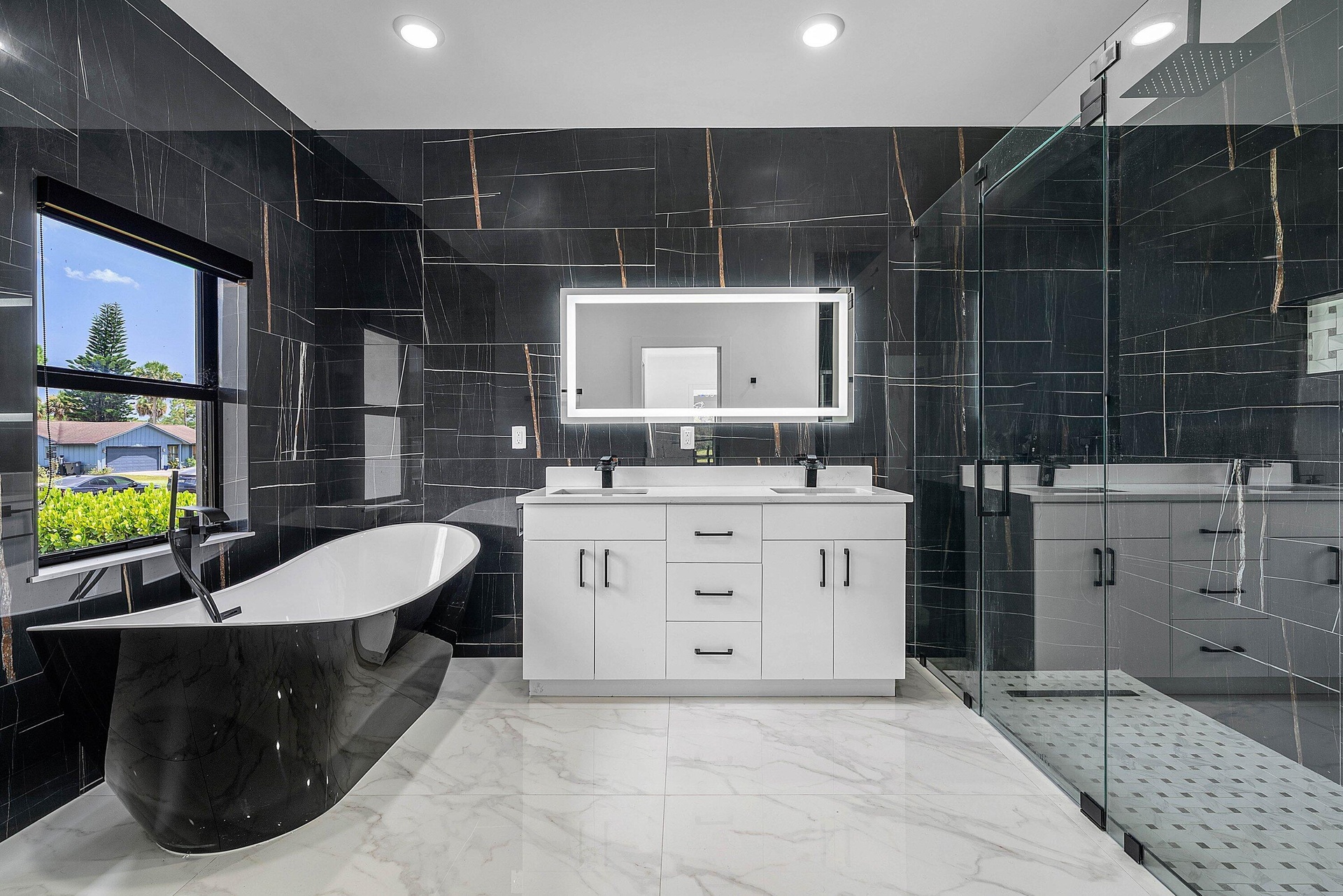 Freestanding soaking tub, dual vanity with undermount sinks, walk-in shower with glass enclosure, large format wall tiling, and recessed lighting