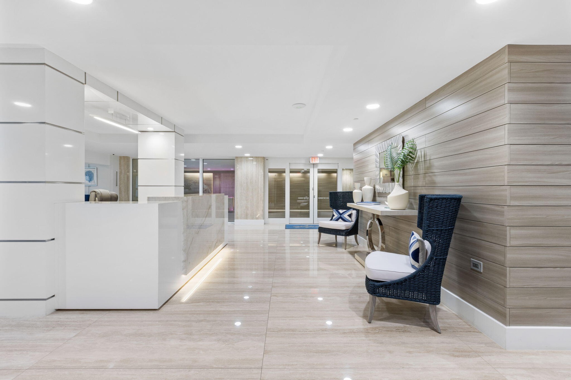 Polished stone flooring, wood-panel accent wall, recessed lighting, white reception desk with stone countertop, and contemporary seating