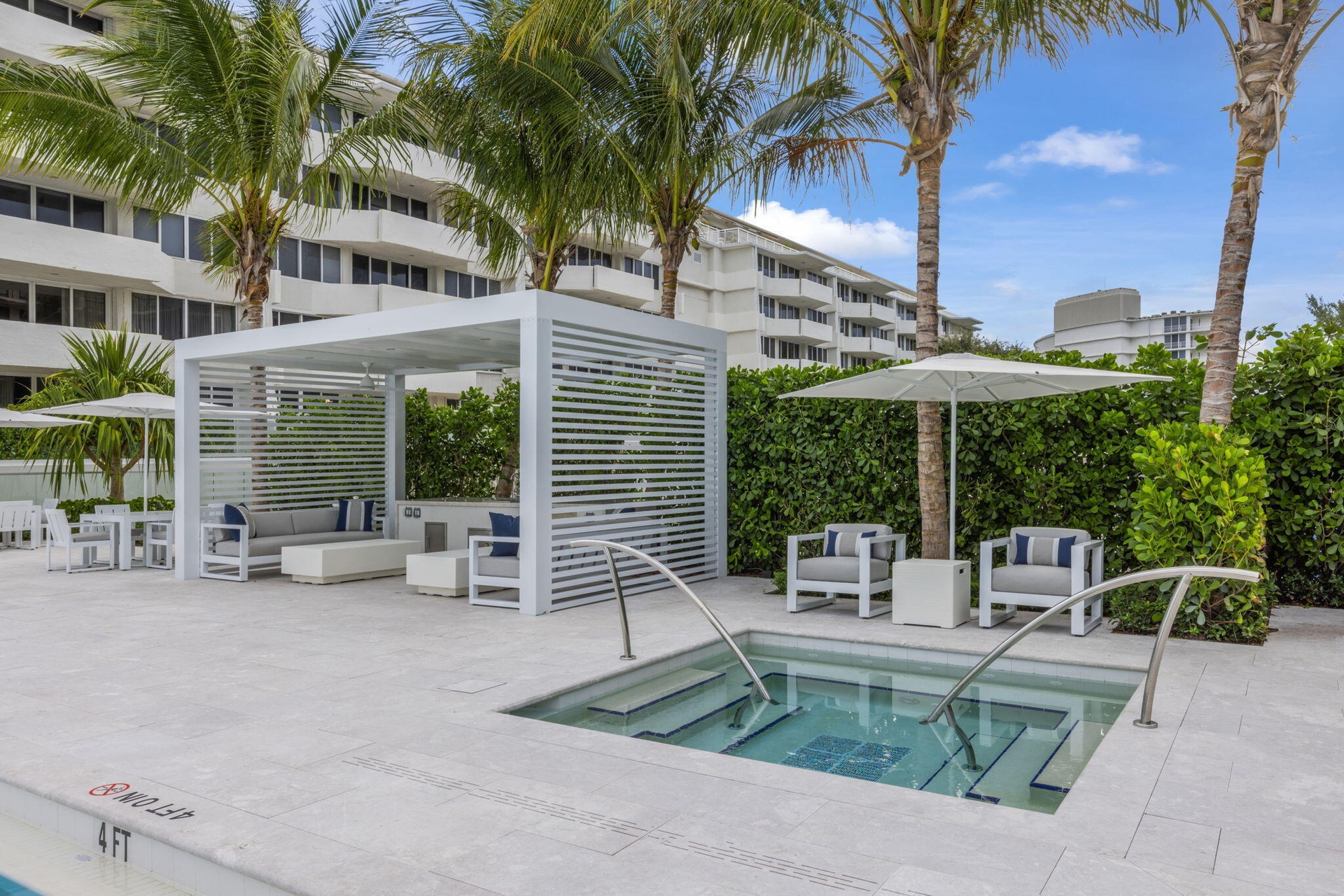 Built-in spa with steps and grab rails, surrounding stone-finish paving, pergola structure, and extensive landscaping