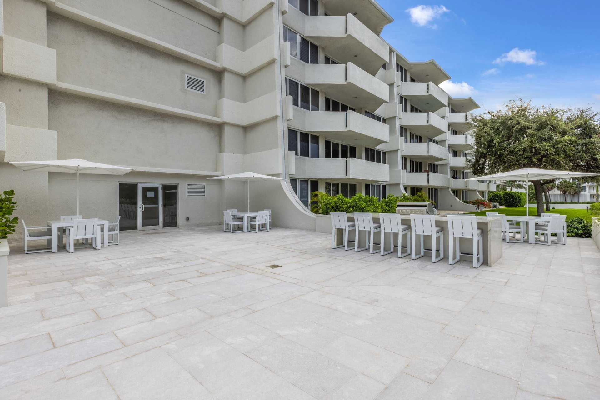 Expansive outdoor patio with stone-finish pavers, multiple seating areas, a built-in bar, and a multi-story building exterior with individual balconie