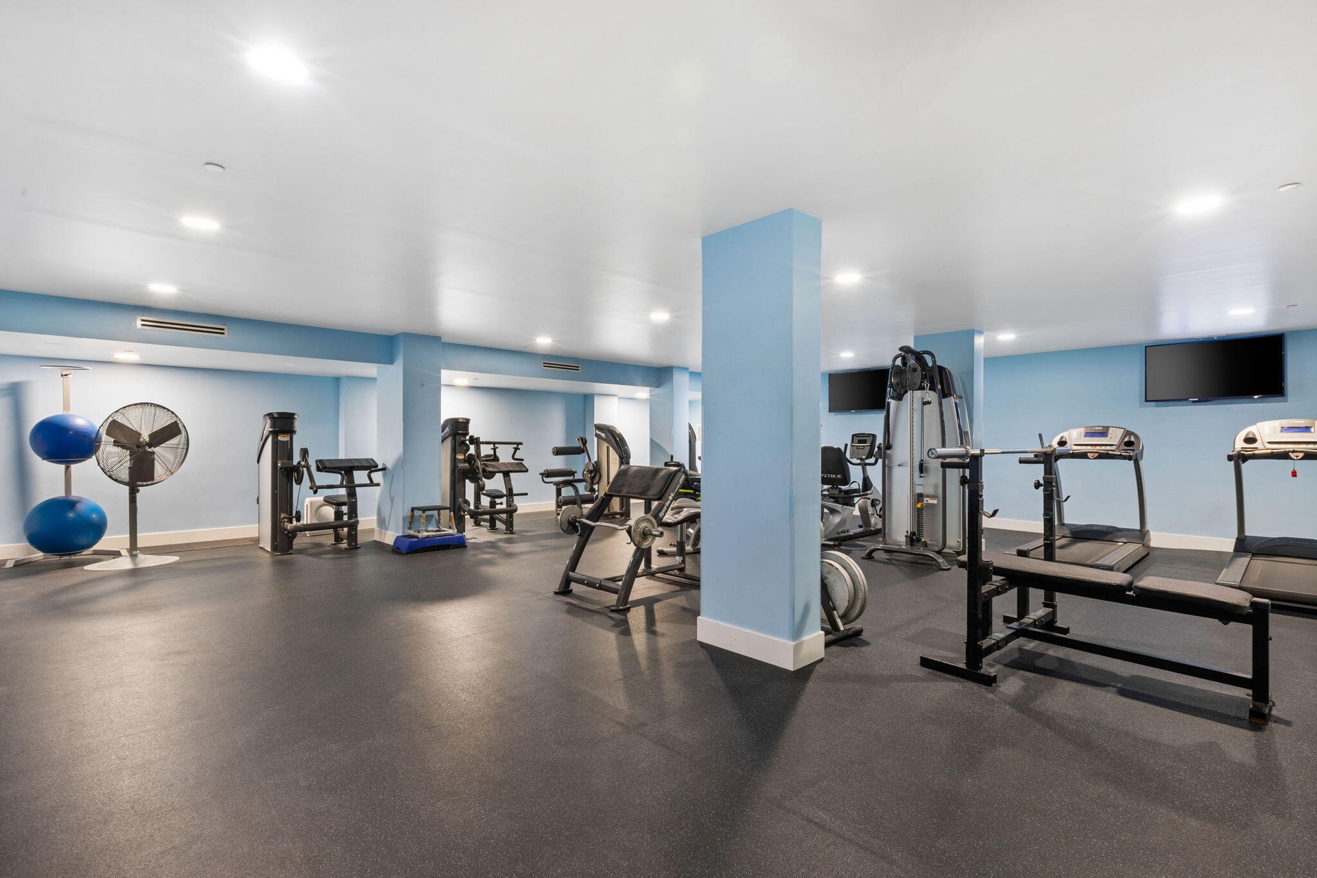 Fitness center with recessed lighting, light blue accent walls, and mounted television screens