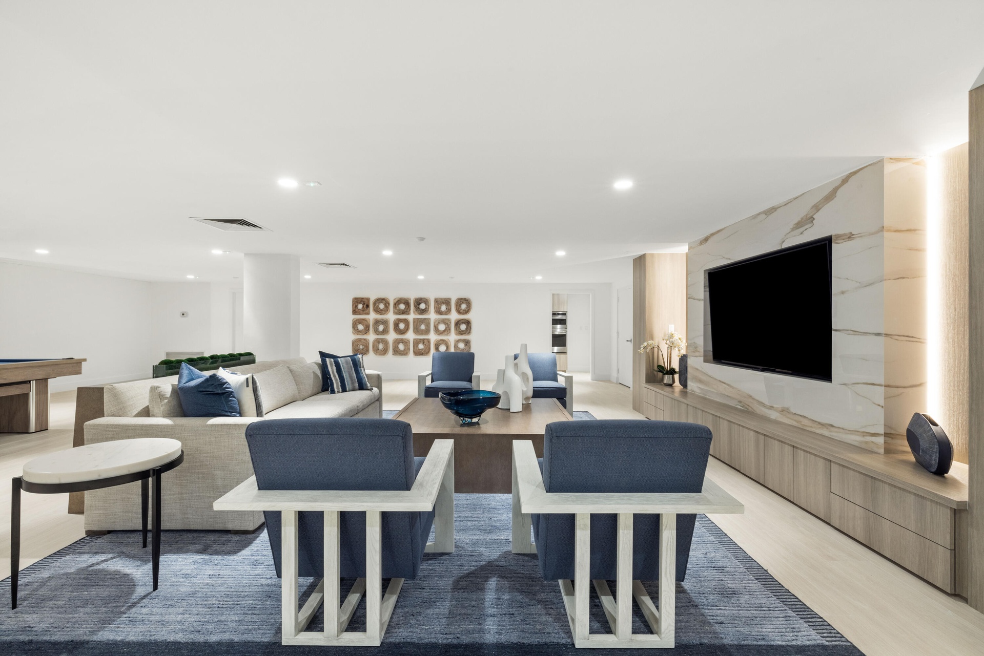 Recessed ceiling lighting, light wood-finish flooring, built-in entertainment unit with integrated lighting, a stone-finish accent wall, and a column-