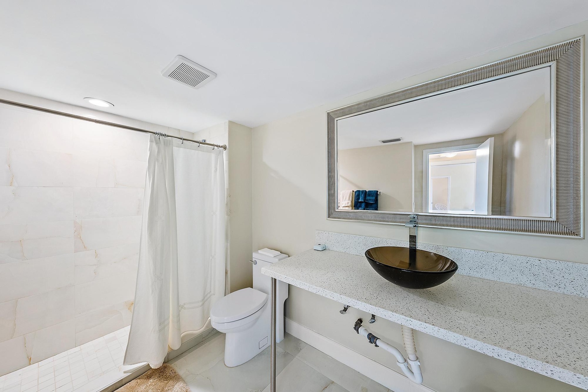 White tile flooring, full wall mirror, glass vessel sink, white countertop, and tiled shower surround