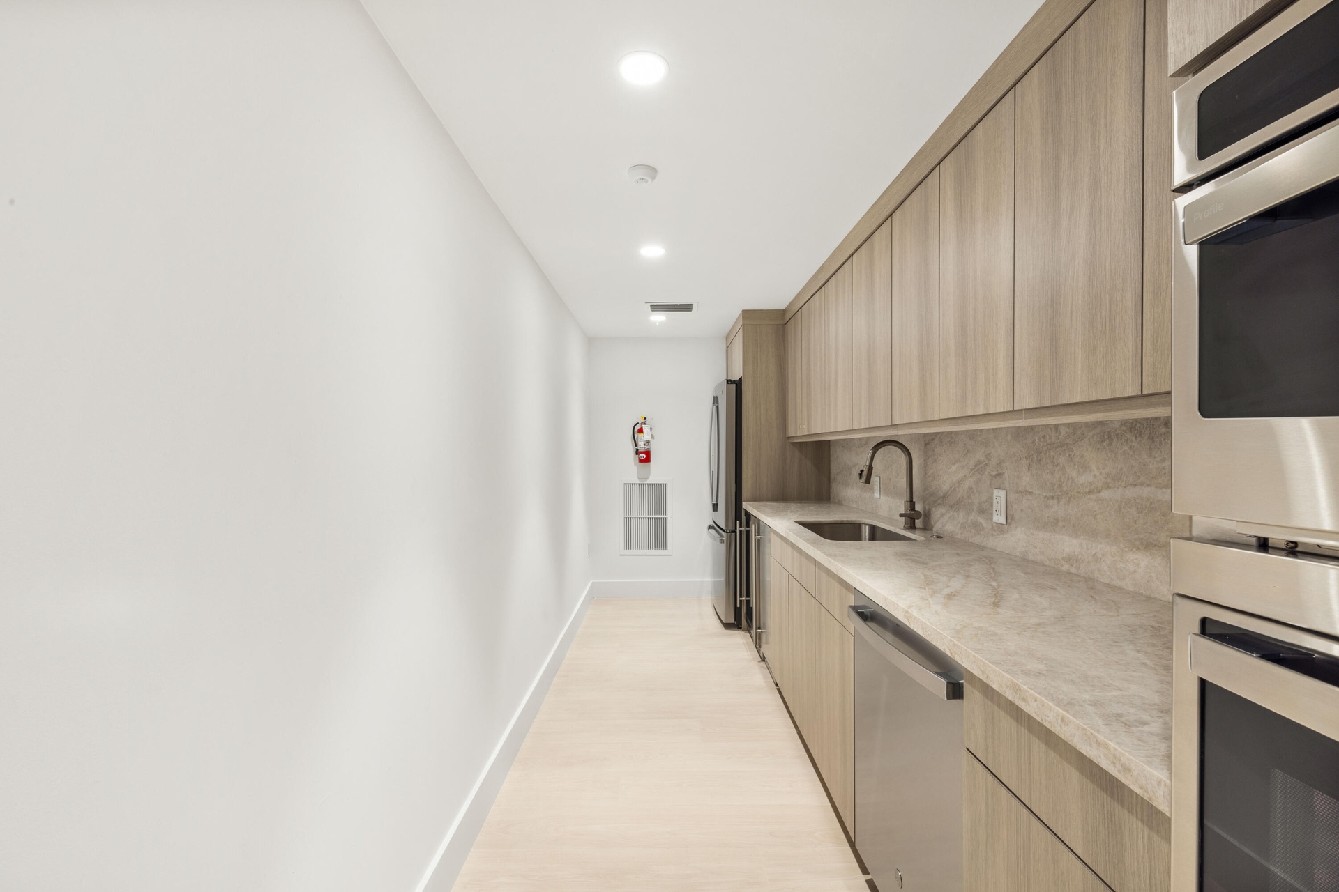 Integrated kitchen area featuring wood-finish cabinetry, stainless steel appliances, a matte black faucet, and stone countertops with a matching backs