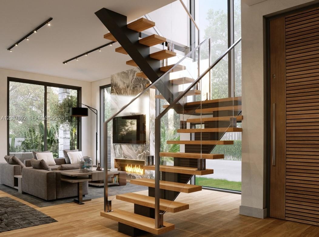 Floating staircase with wood treads and glass railing, wide plank wood-finish flooring, full-height windows, built-in fireplace with stone surround, a