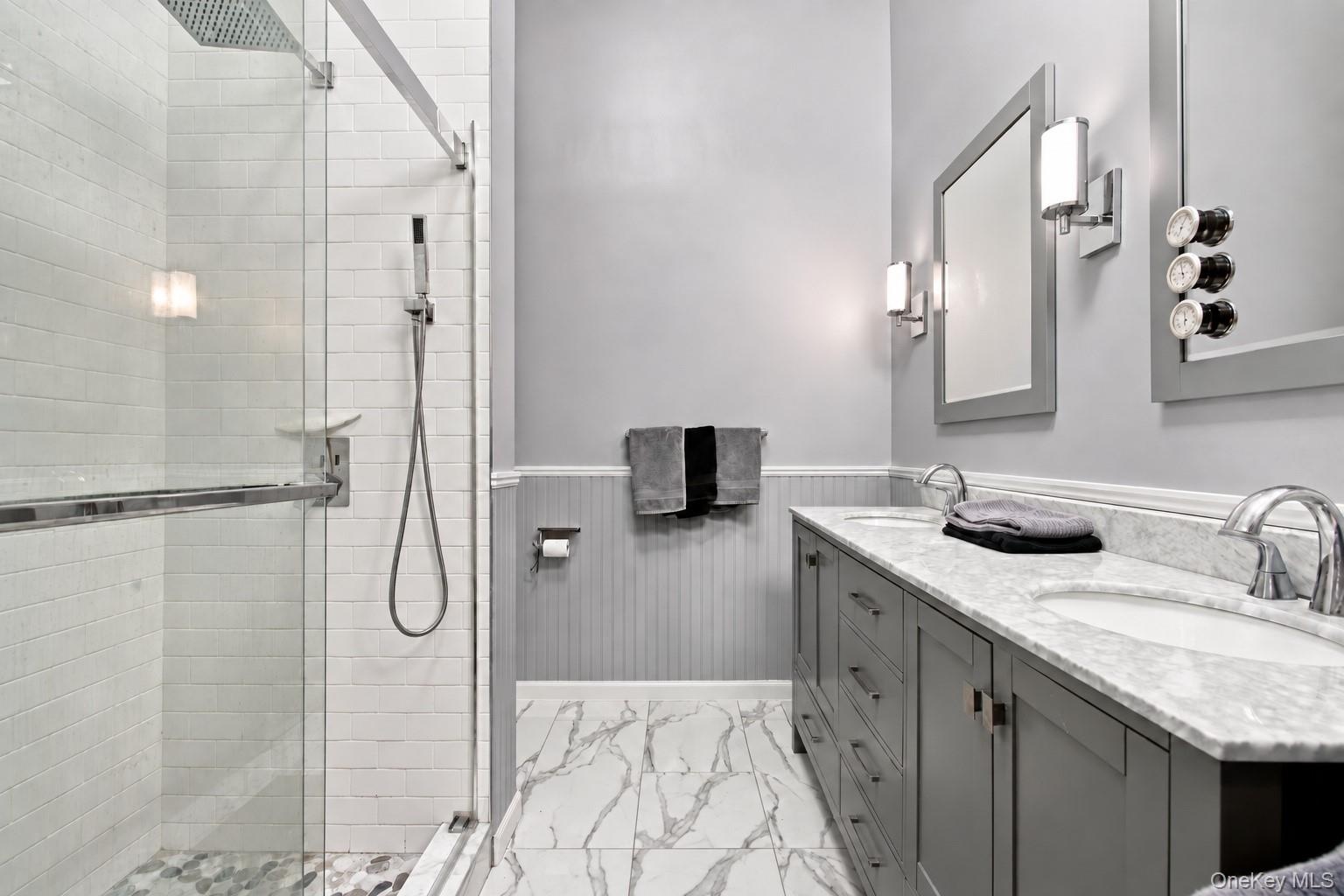 Modern bath w/dual sink vanity with stone countertop, glass-enclosed shower and marble floors