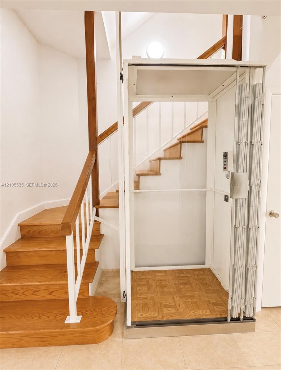 Built-in home elevator with patterned wood-finish flooring, staircase with wood treads, and white wall paneling