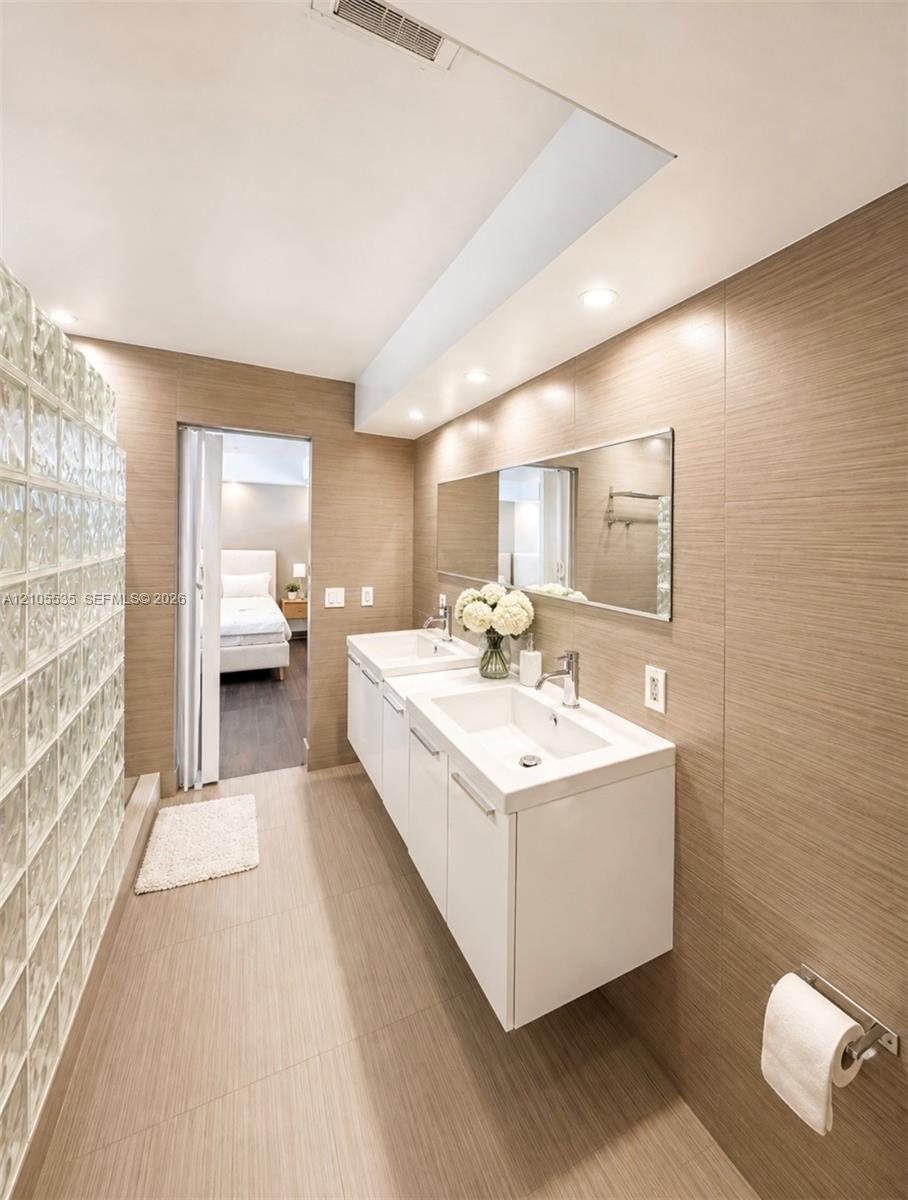 Dual floating vanities with integrated sinks, recessed lighting, glass block wall, and large wall-mounted mirror