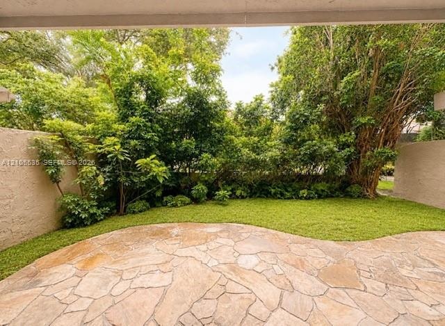 Paved patio area with flagstone-style surfacing, surrounded by a manicured lawn and mature landscaping, featuring lush green foliage