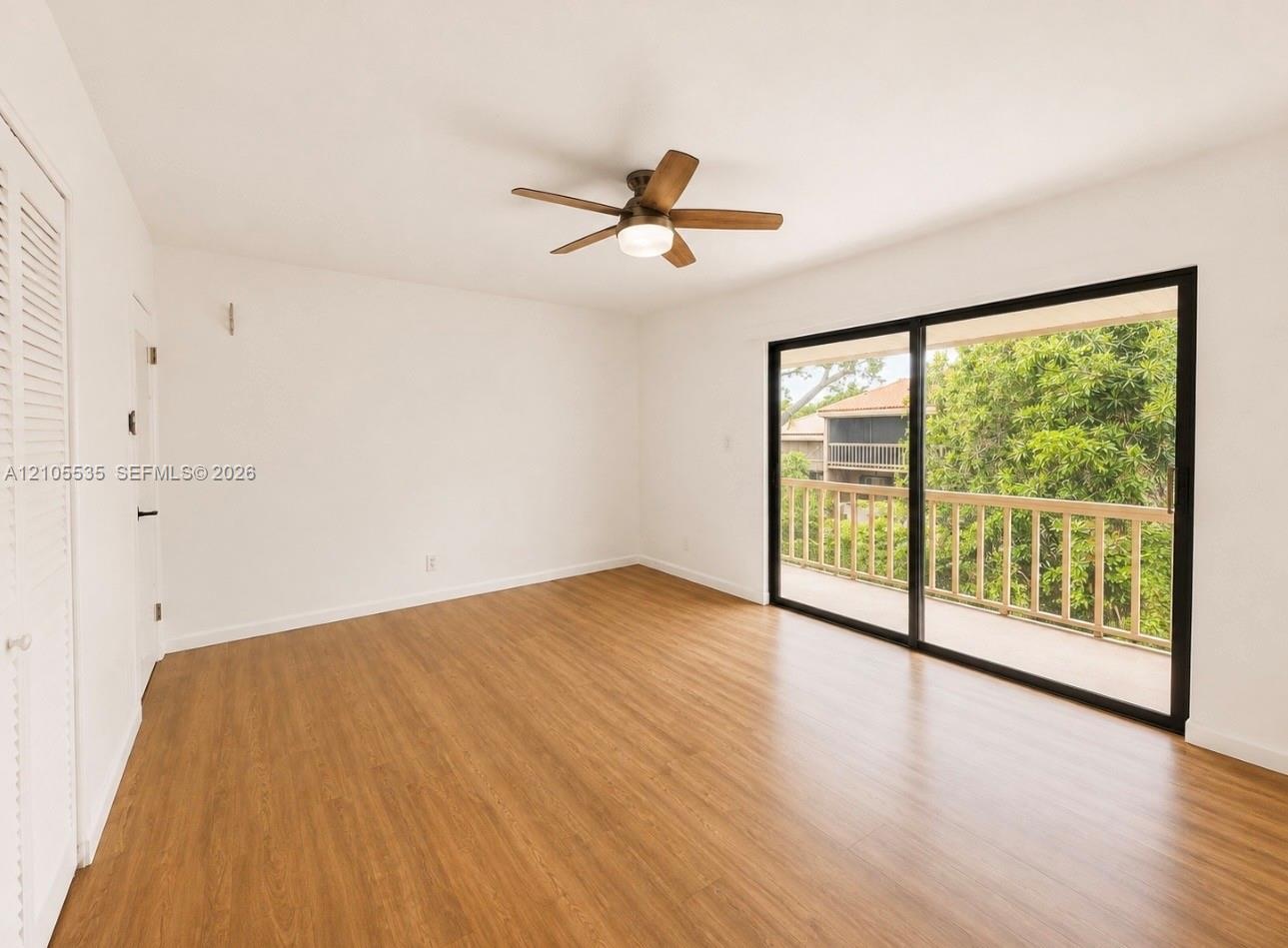 Wood-finish flooring, sliding glass doors, private balcony with wood railing, ceiling fan with integrated lighting, and louvered bifold closet doors
